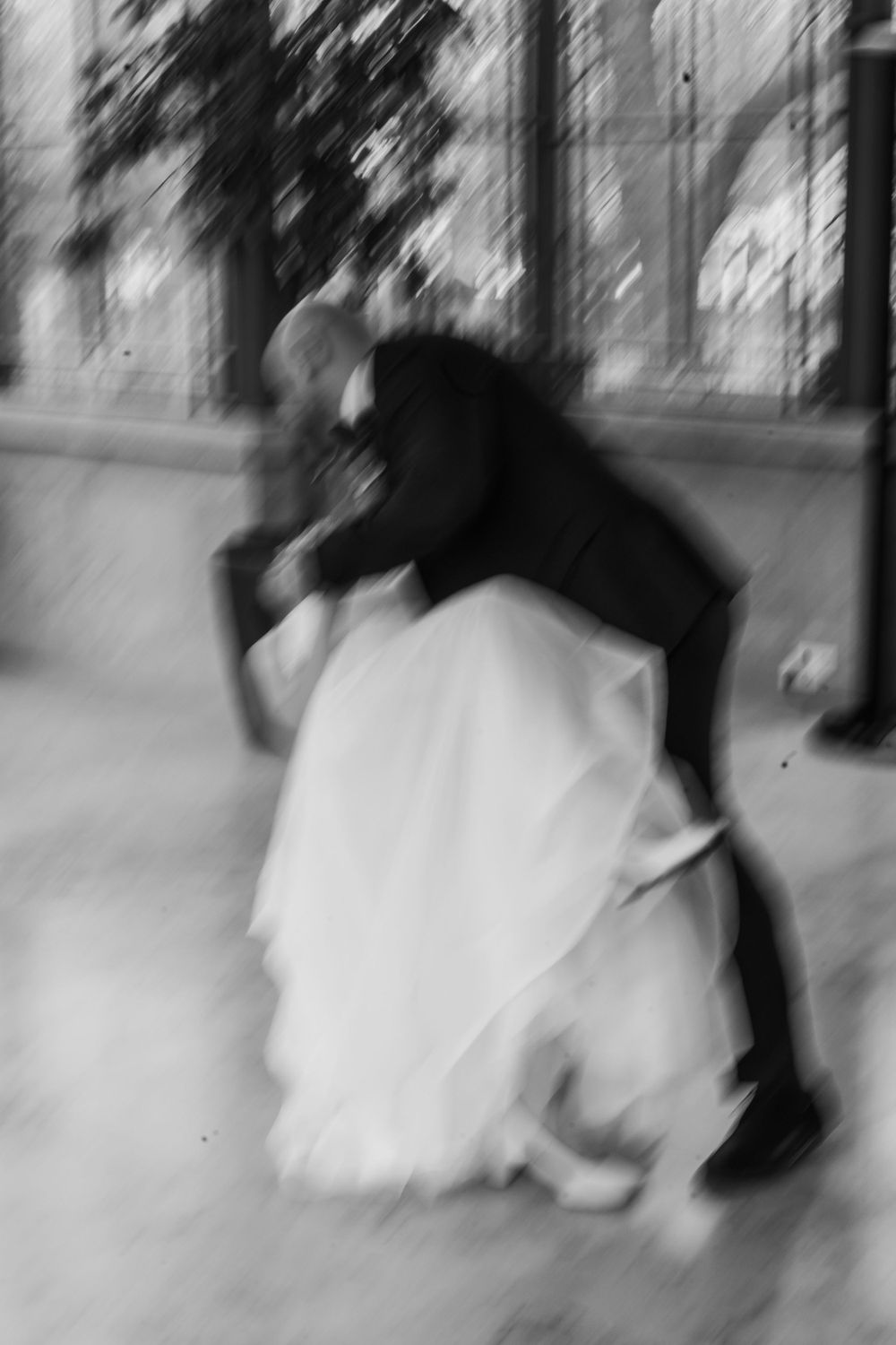 A black and white motion-blurred photograph of a couple dancing, with the woman wearing a flowing white dress.