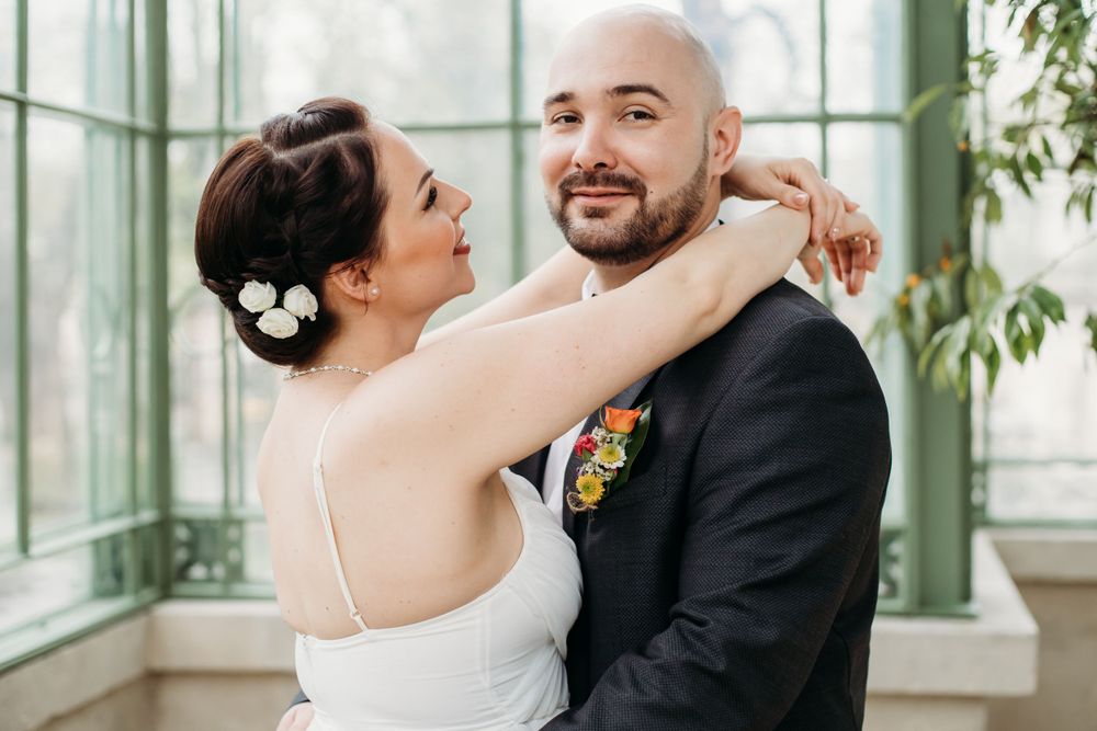 Newlyweds share a joyful embrace during their wedding photoshoot in a bright, sunlit greenhouse.