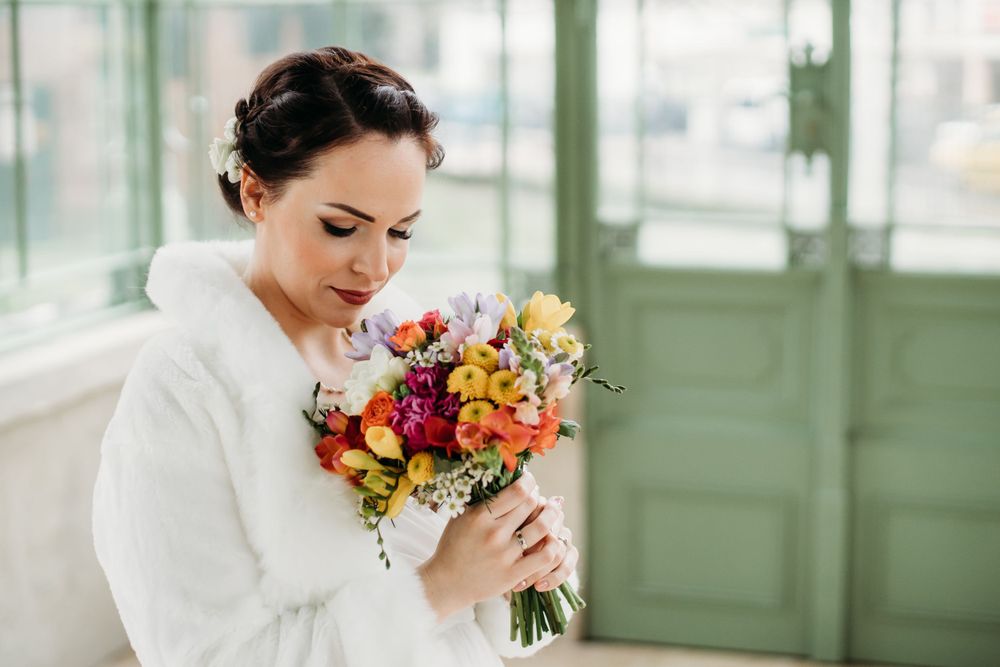 Person in white cozy robe holding vibrant autumn-colored bouquet of flowers in sunlit room with green walls.