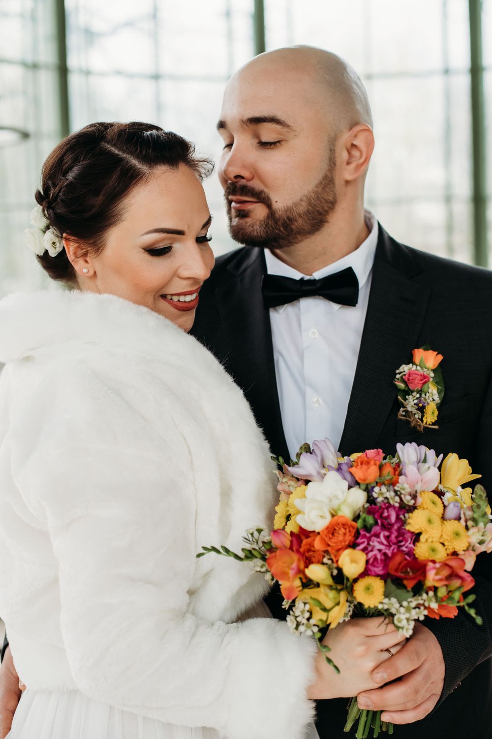 A romantic winter wedding moment featuring a plush white fur wrap and vibrant colorful bouquet with orange and yellow blooms.