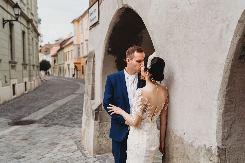 A romantic wedding couple embraces in an arched doorway along a charming cobblestone street in Europe.