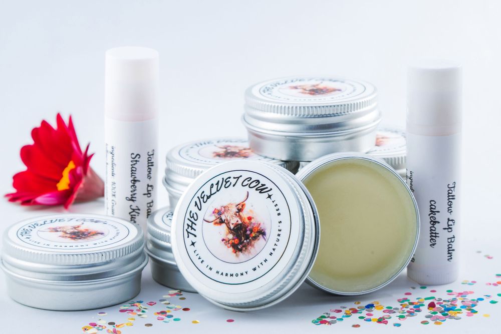 Small jars of handmade body balm with white lids and custom labels displayed with a red flower and colorful confetti.
