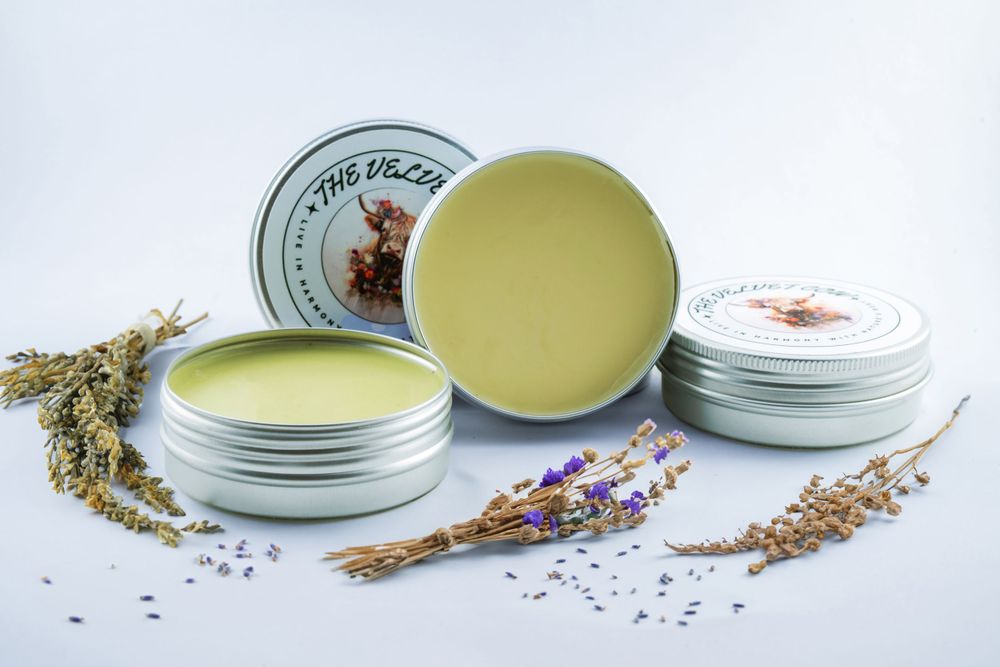 Natural healing balm tins surrounded by dried lavender and herbs on a white surface.