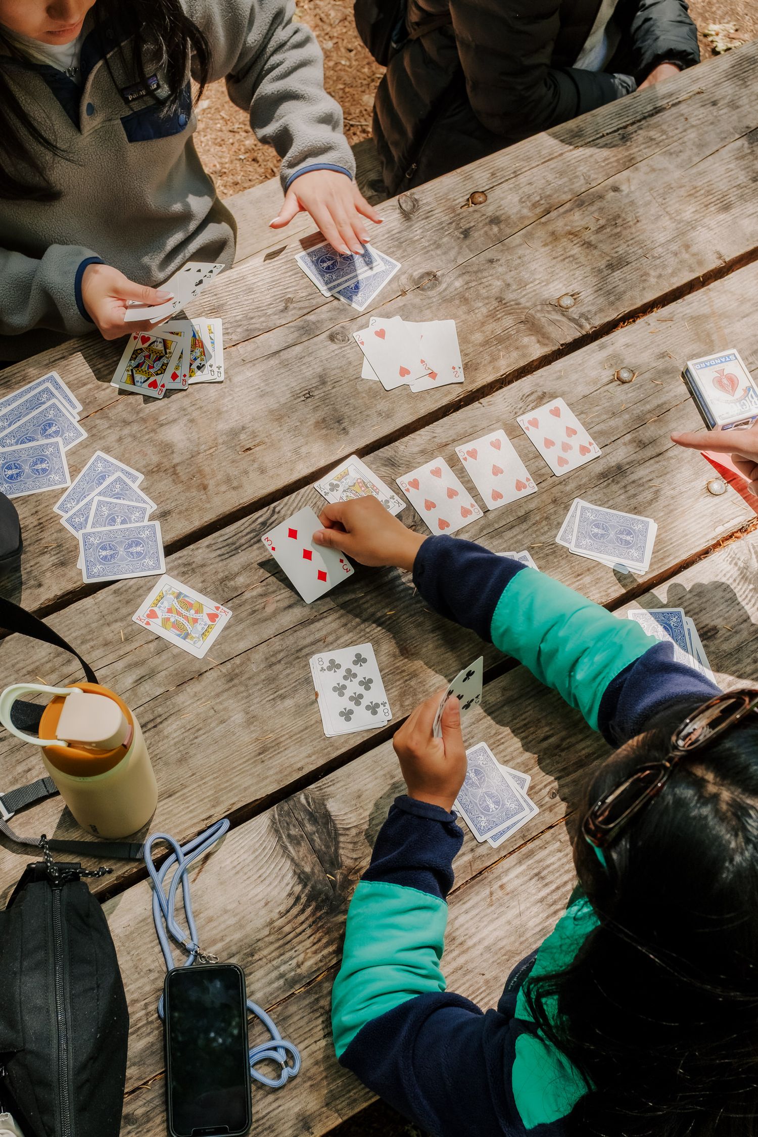 People playing cards on a rustic wooden picnic table with a coffee mug nearby on a casual afternoon.