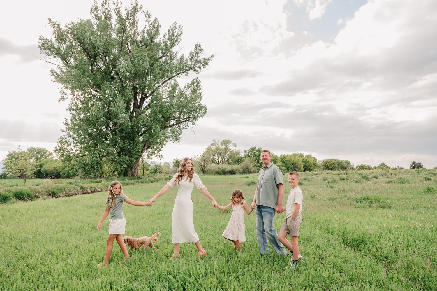 Family holding hands while walking through a lush green meadow on a cloudy summer day.