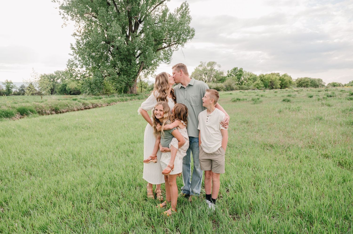 A group stands together in a serene grassy meadow with a tall tree in the background on a cloudy summer day.