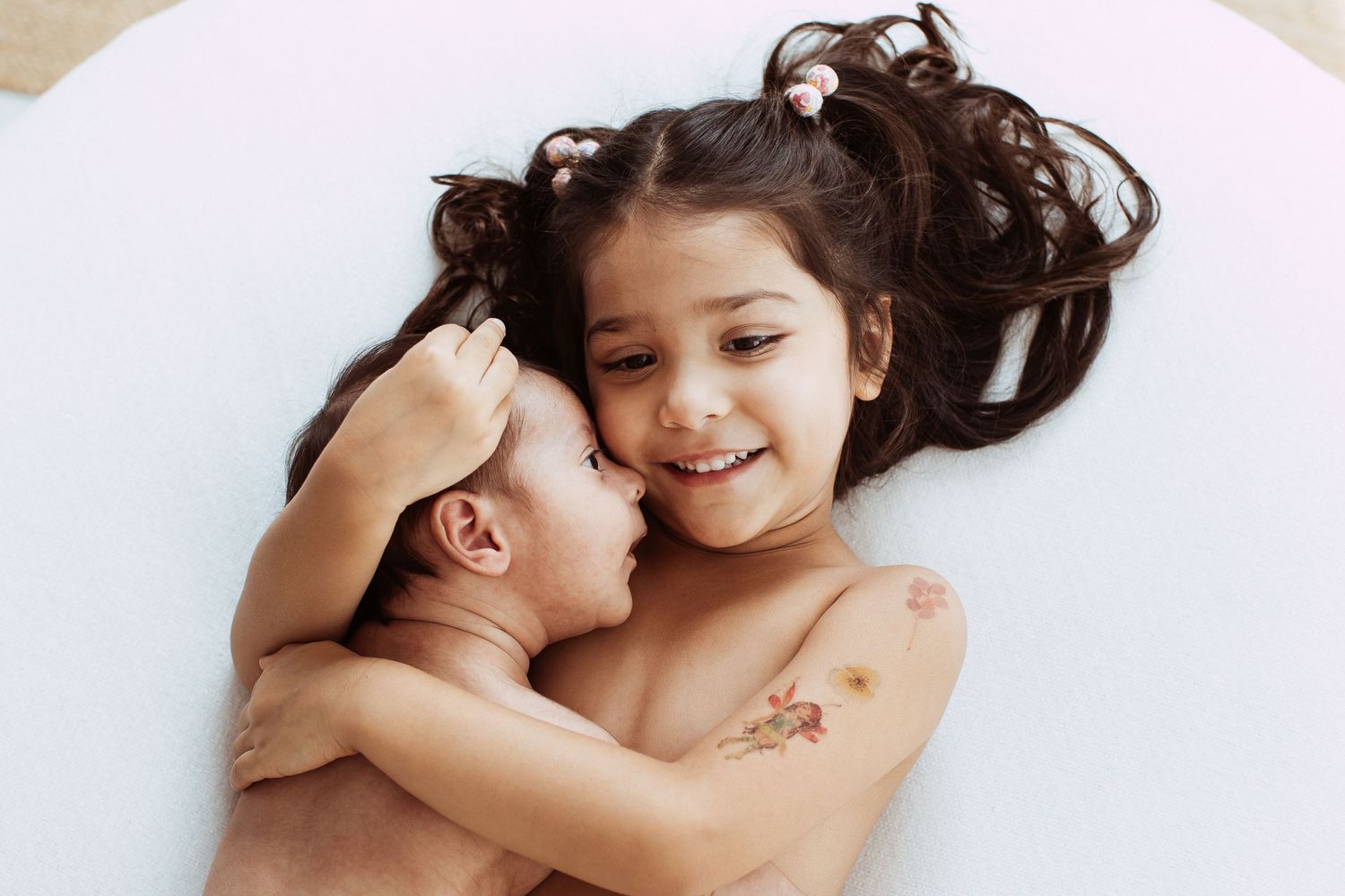 Two young children sharing a sweet moment on white bedding.