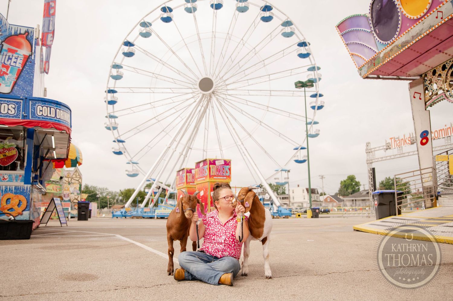 Two goats pose in front of a large ferris wheel at a carnival fair.
