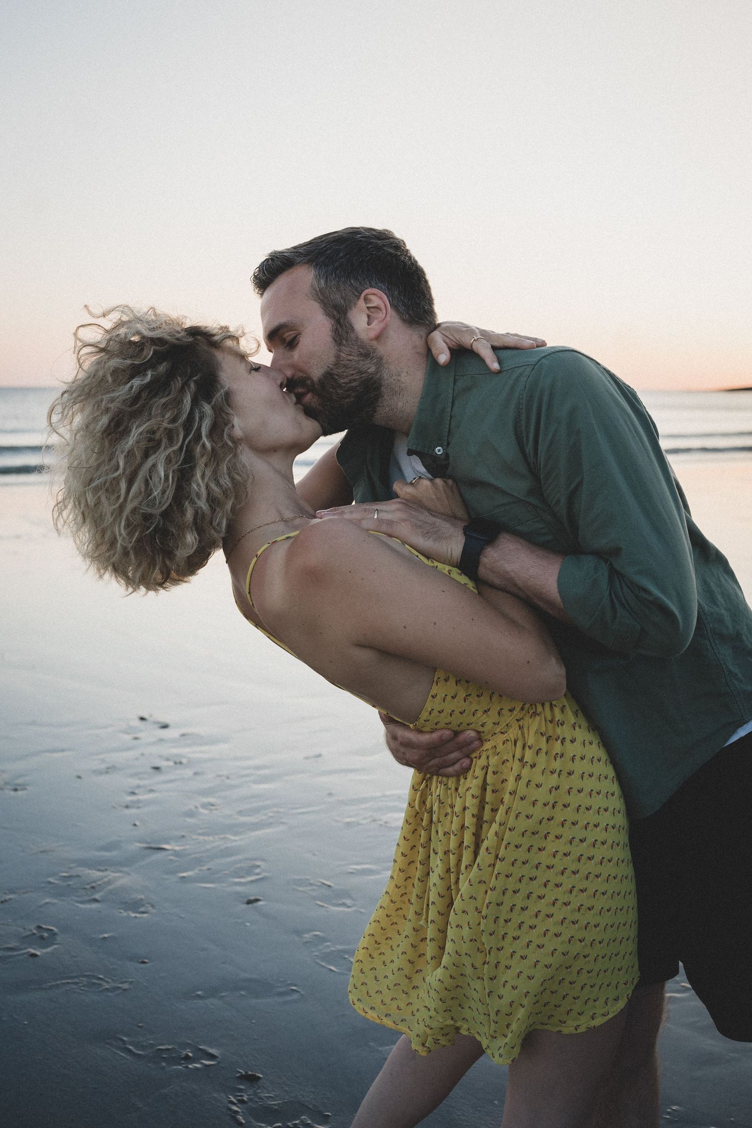 Romantic couple sharing a passionate kiss on the beach at sunset.