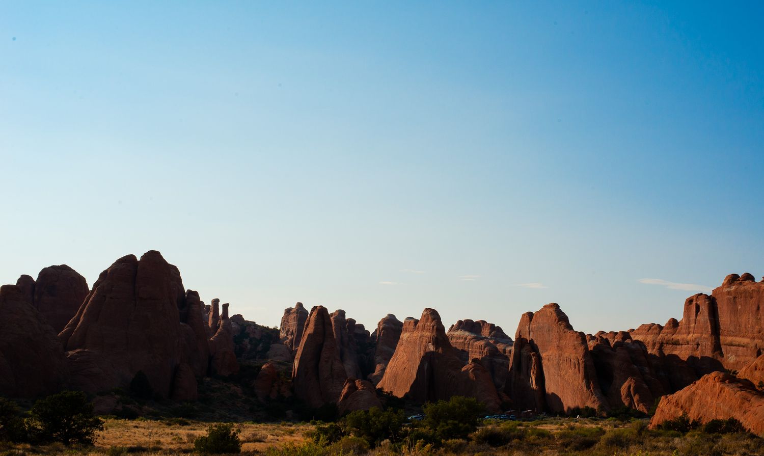 Dramatic red rock formations silhouetted against a clear blue sky in a desert landscape at dusk.