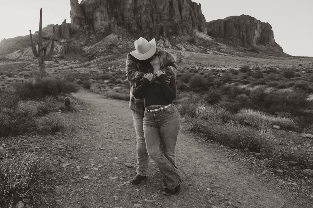 A black and white photo of a couple kissing in the Tonto National Forest at the base of the Superstitions.