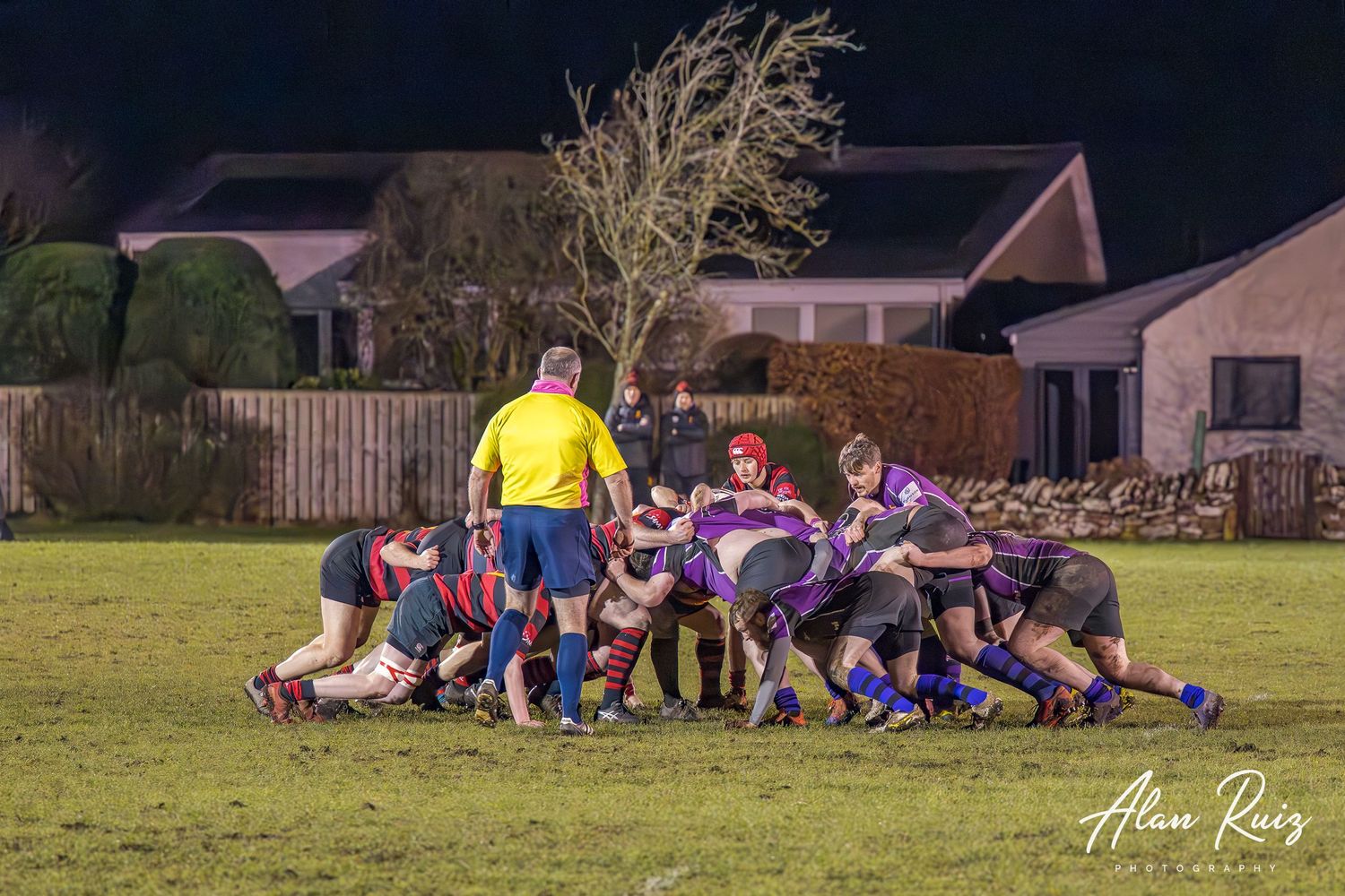 Rugby team huddles together on a grass field during sunset.
