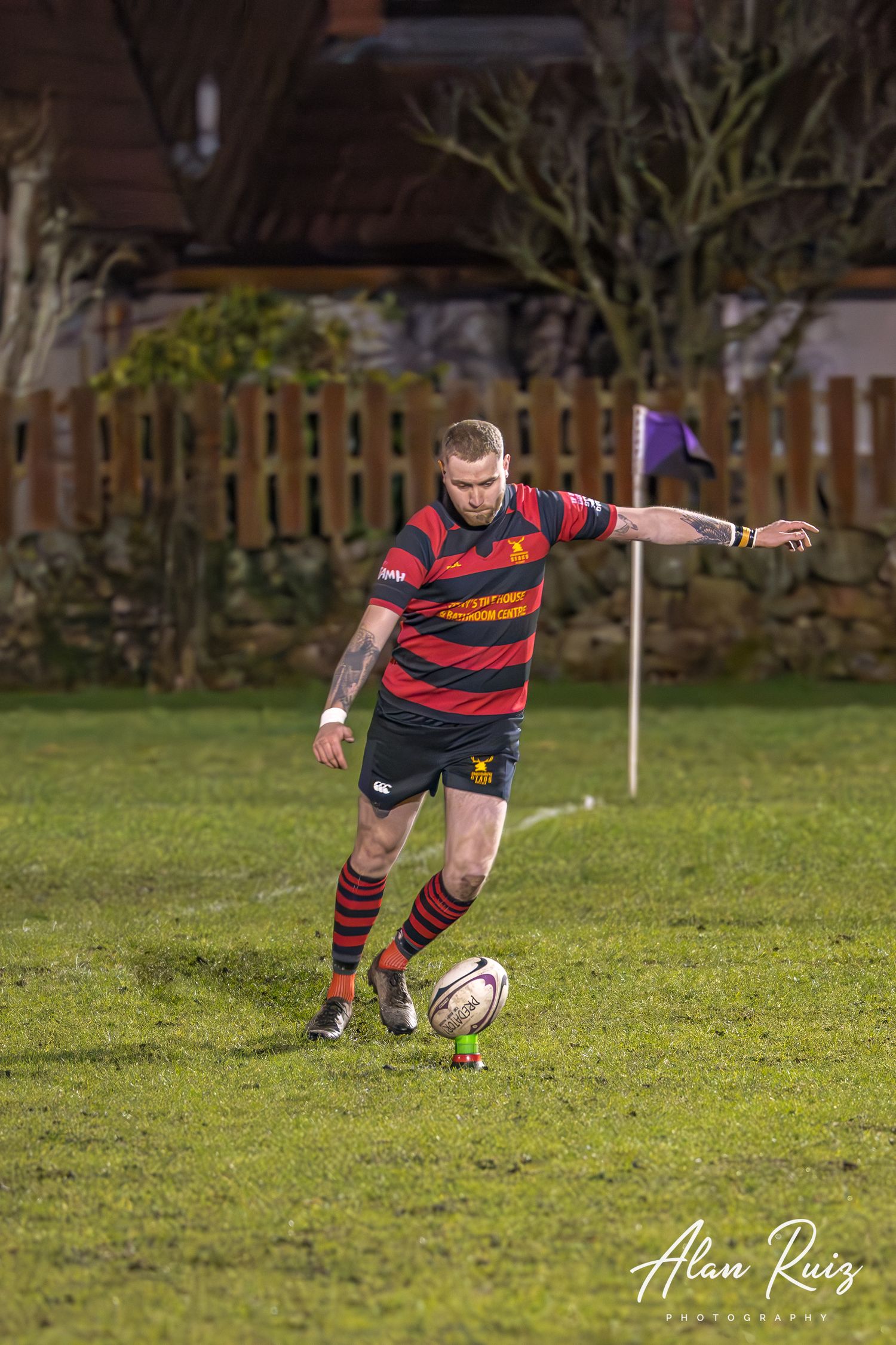 Rugby player in striped jersey prepares to kick the ball on a grass field.