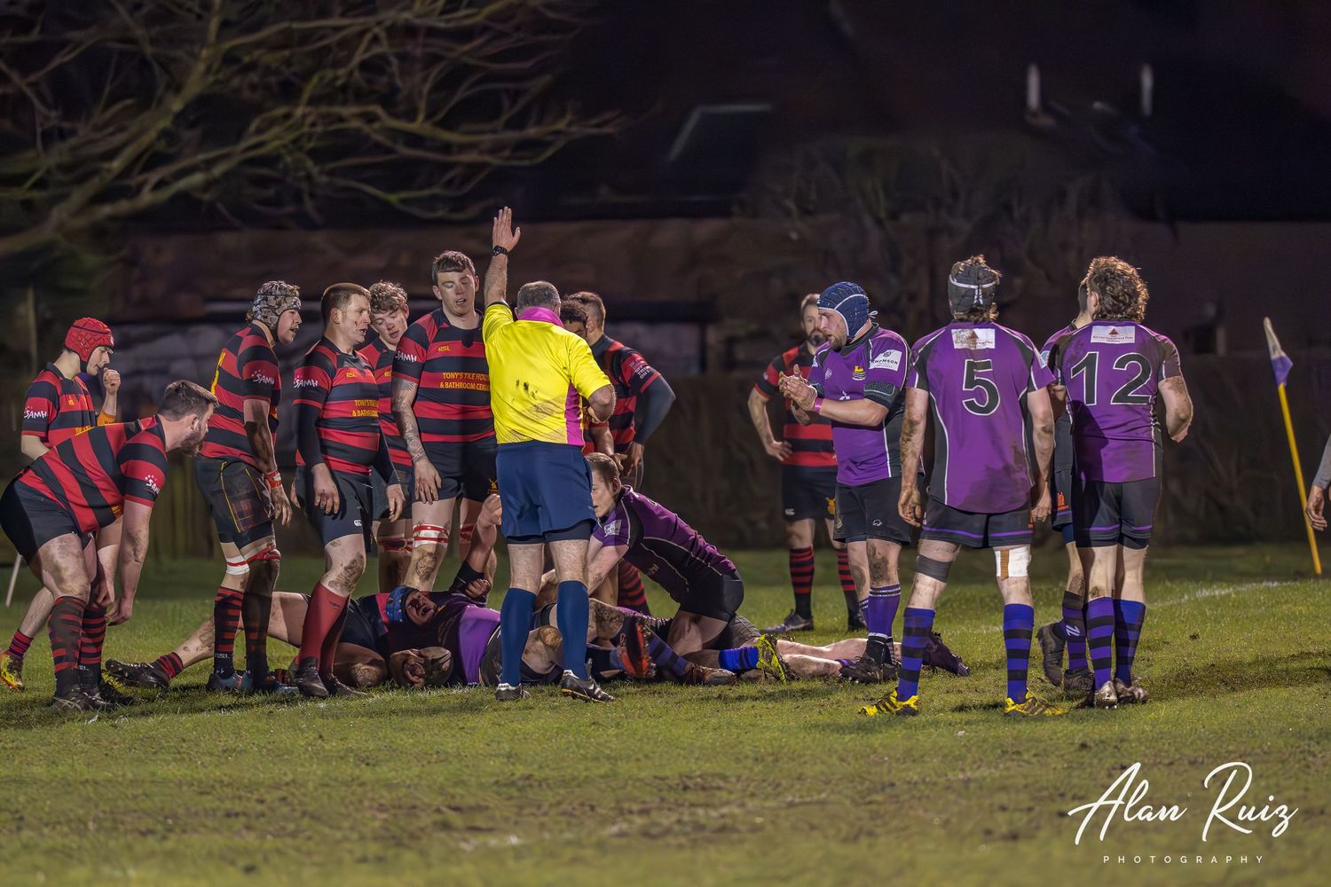 Rugby teams compete during a nighttime match on a floodlit field.
