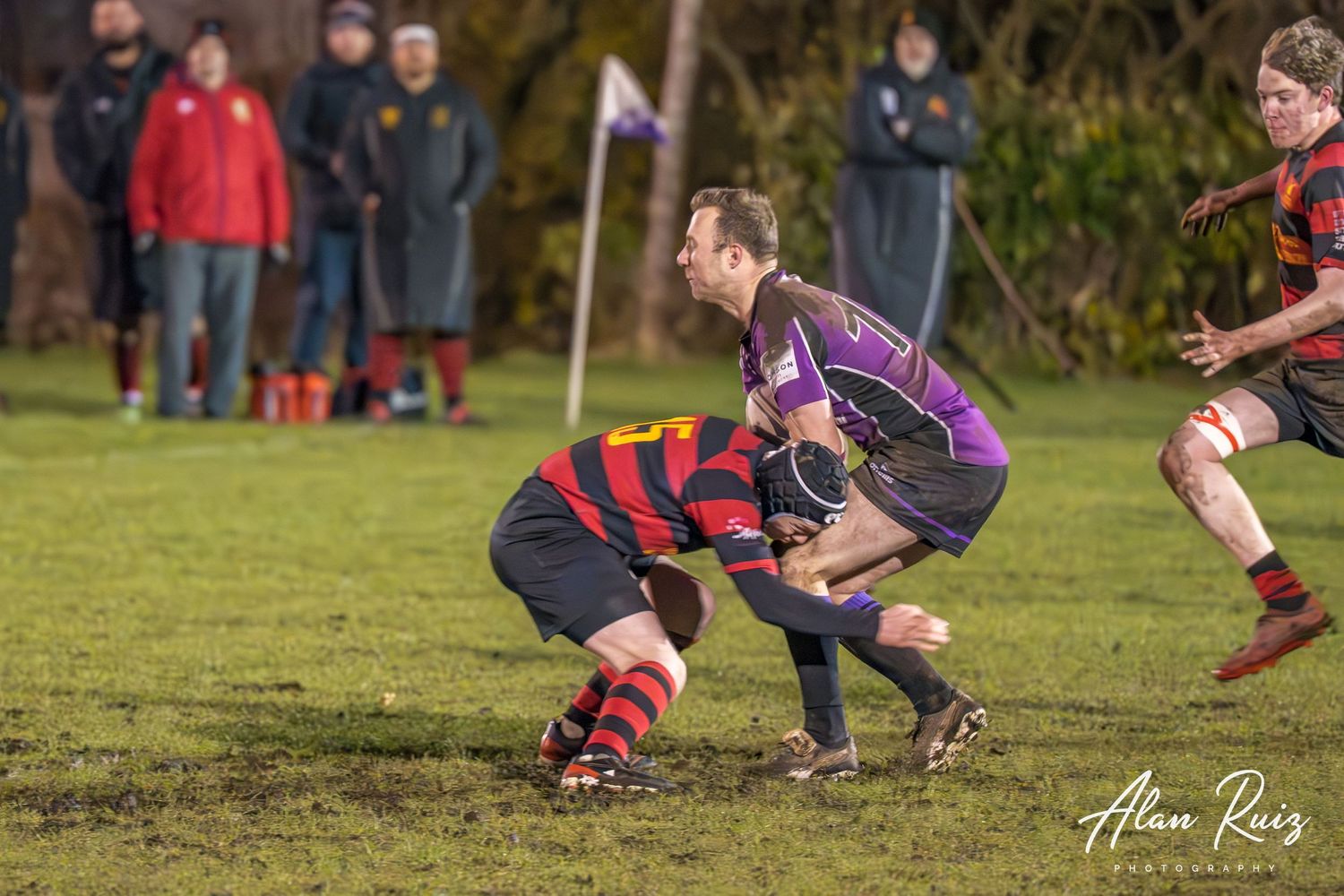 Rugby players engage in a close ground battle during a competitive match on a muddy field.