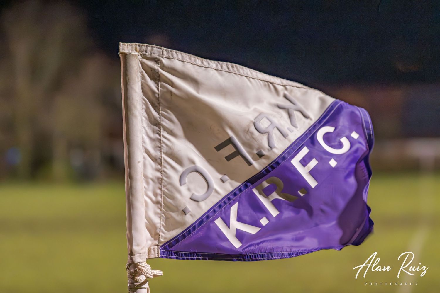 Close-up of a purple and white rugby flag waving against a dark background.