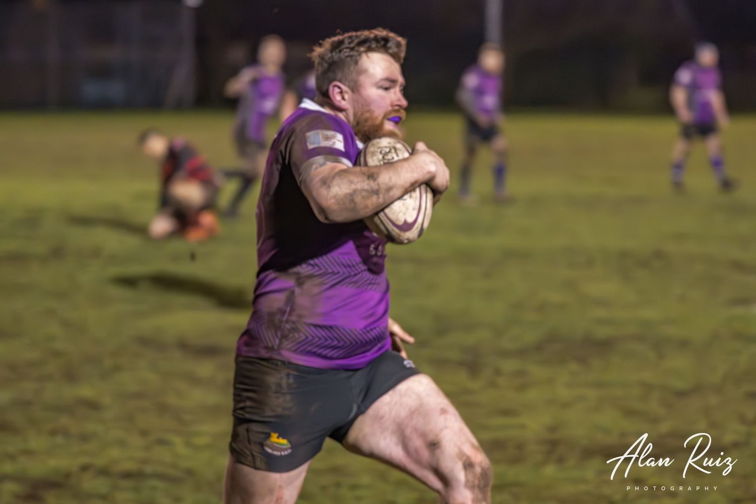 Rugby player carries the ball while running through defenders on the field.