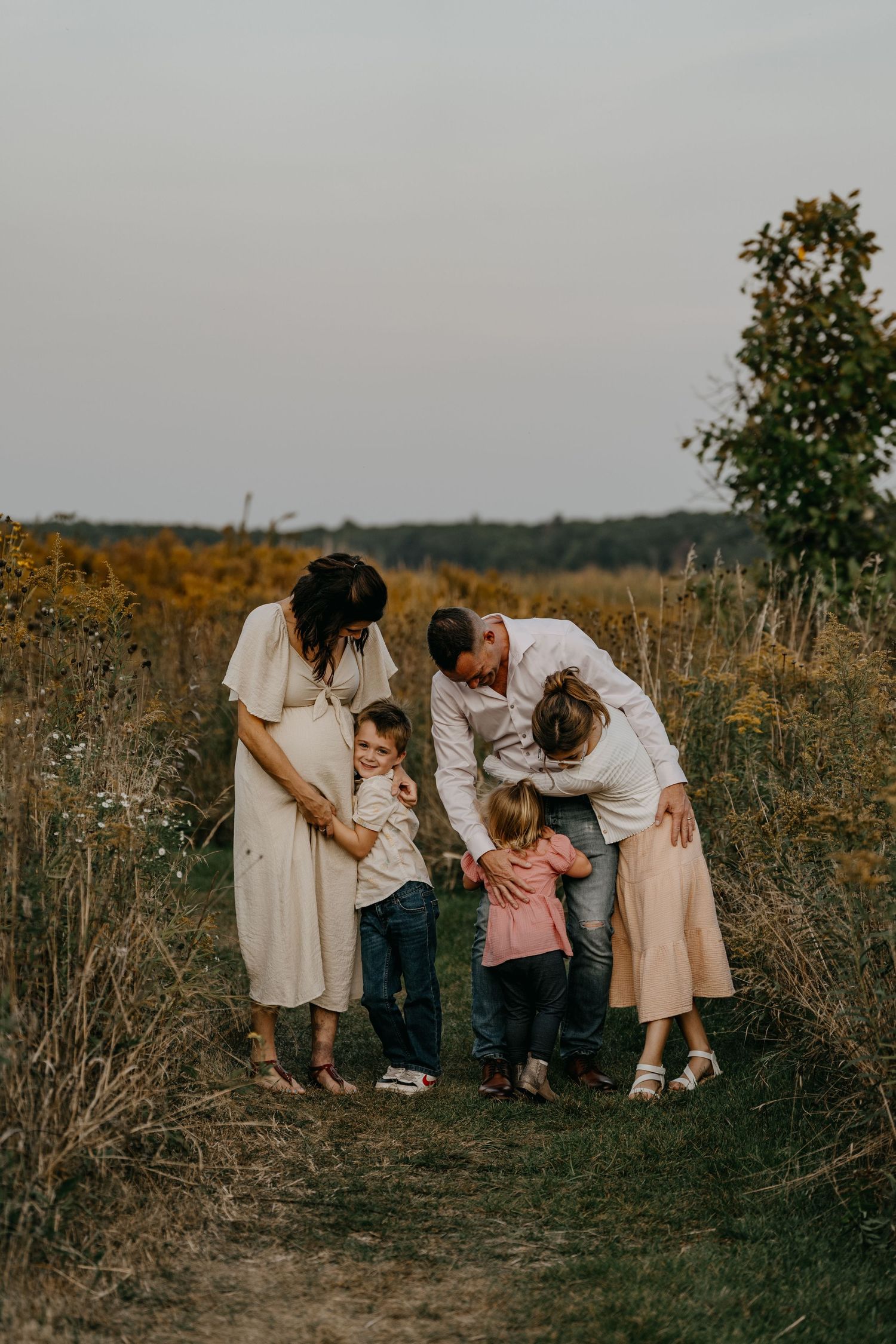 A group enjoys a tender moment together on a path surrounded by wildflowers at dusk in matching white outfits.