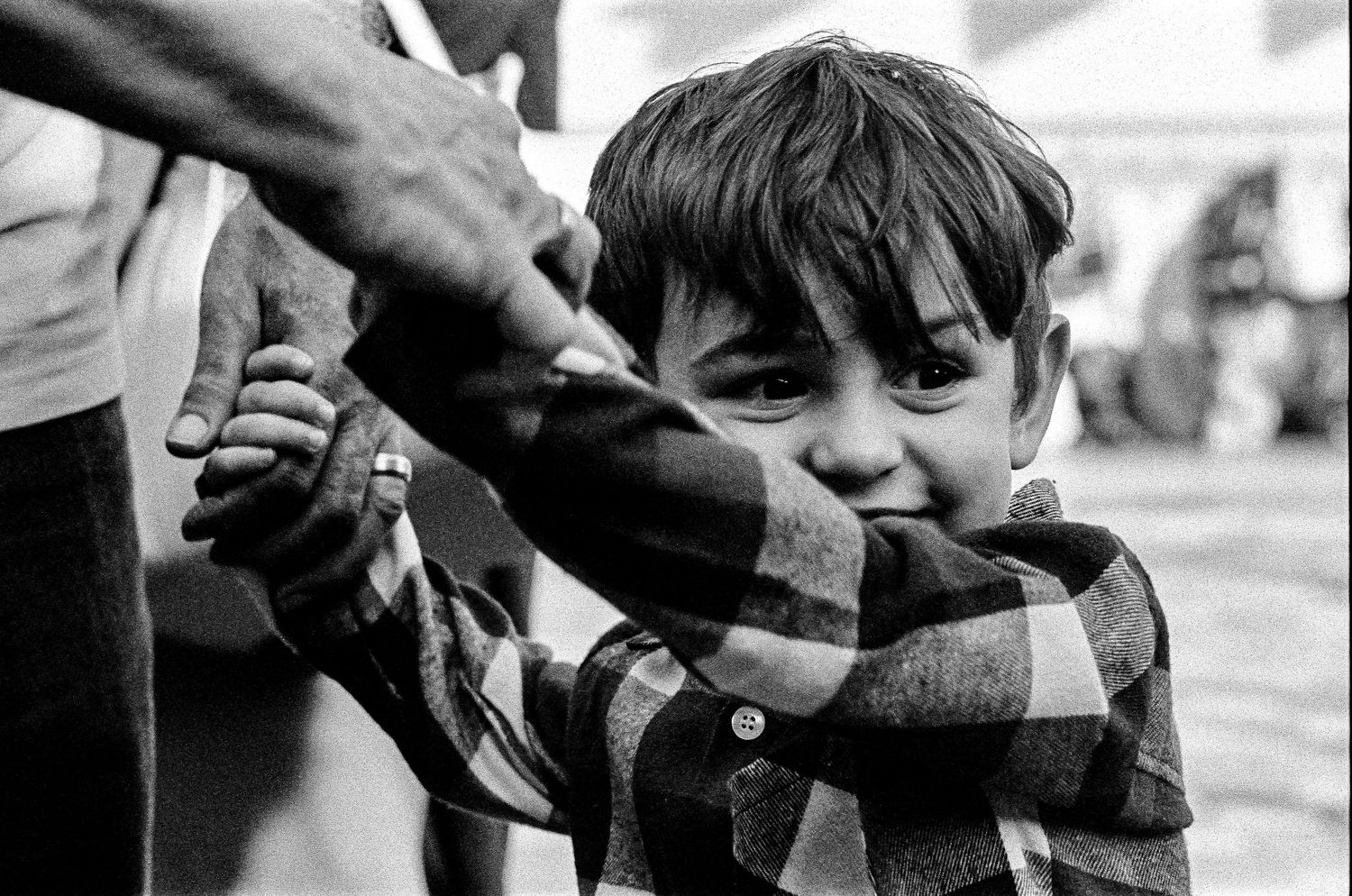 Black and white photo showing a child wearing a plaid coat being comforted by an adult's hand on their head.