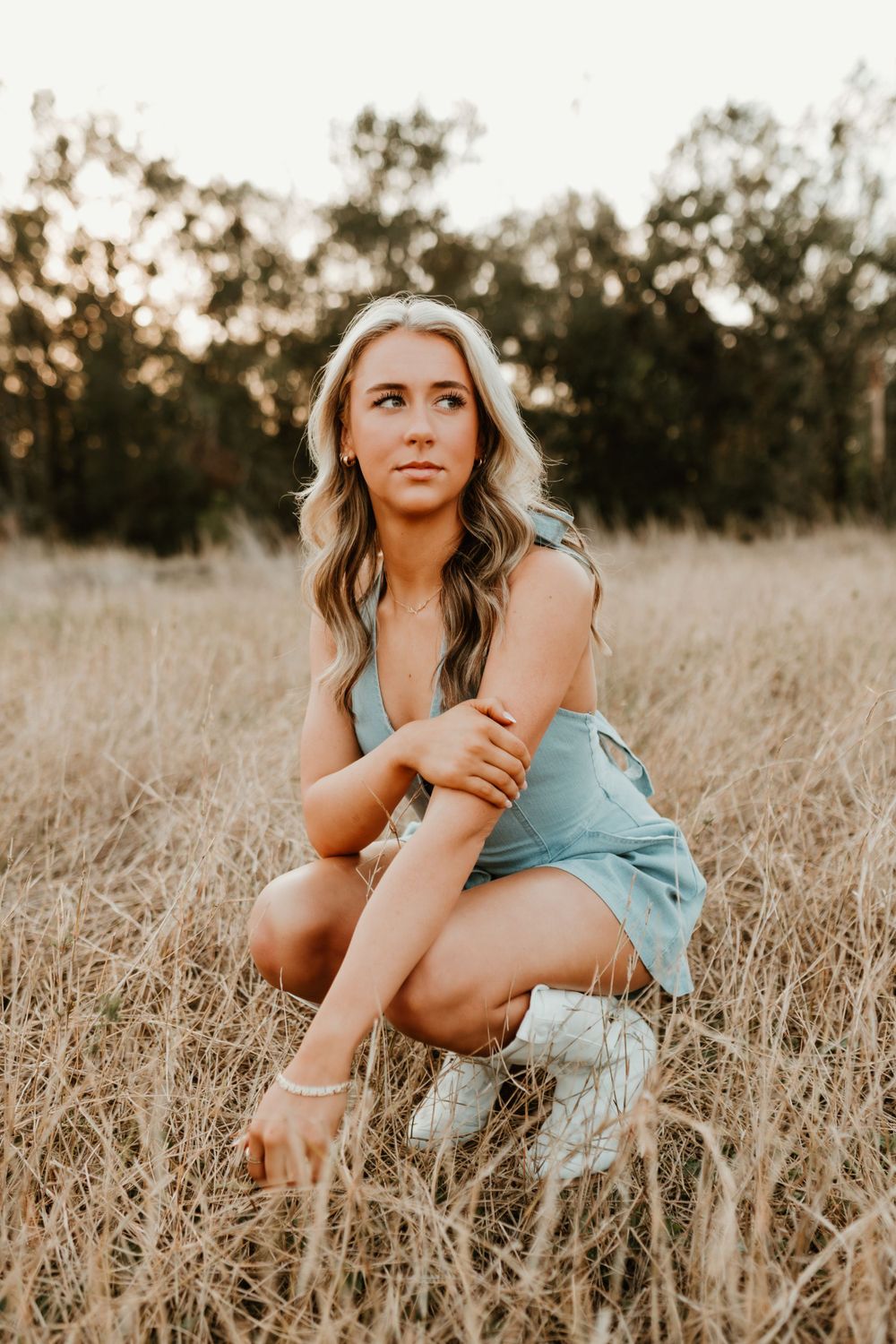 Person in a turquoise romper poses playfully in a golden wheat field at sunset.