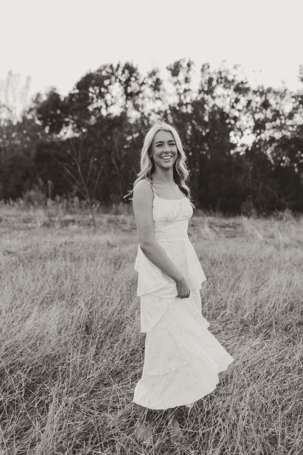 Person in white dress twirls joyfully in a field at sunset.