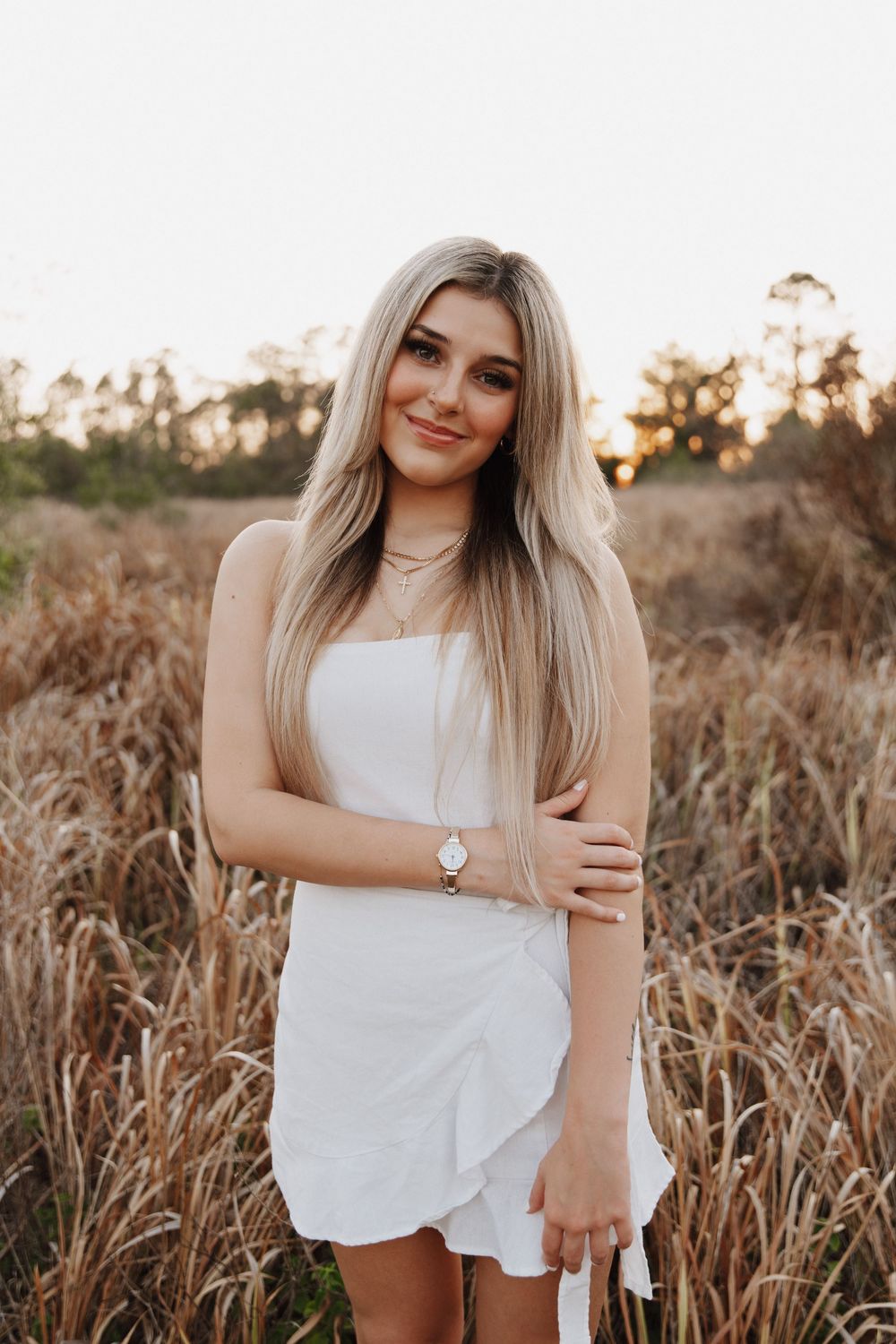 A woman in a white top posing in a golden wheat field at sunset during a summer photoshoot.