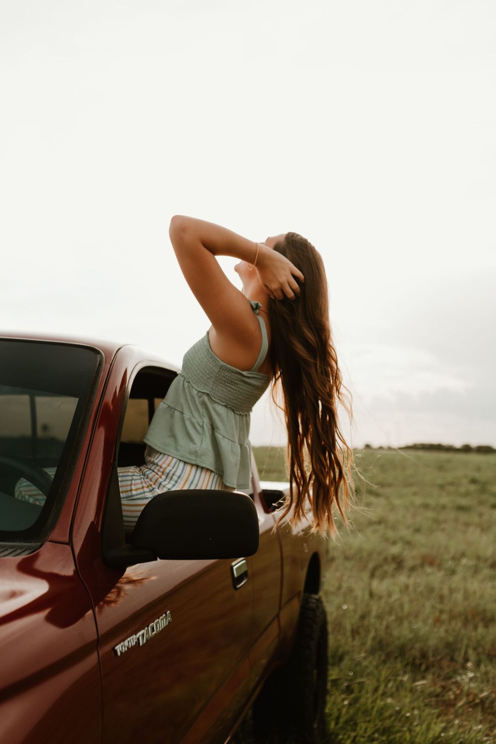 Person leans back on vintage red truck in rural field setting.