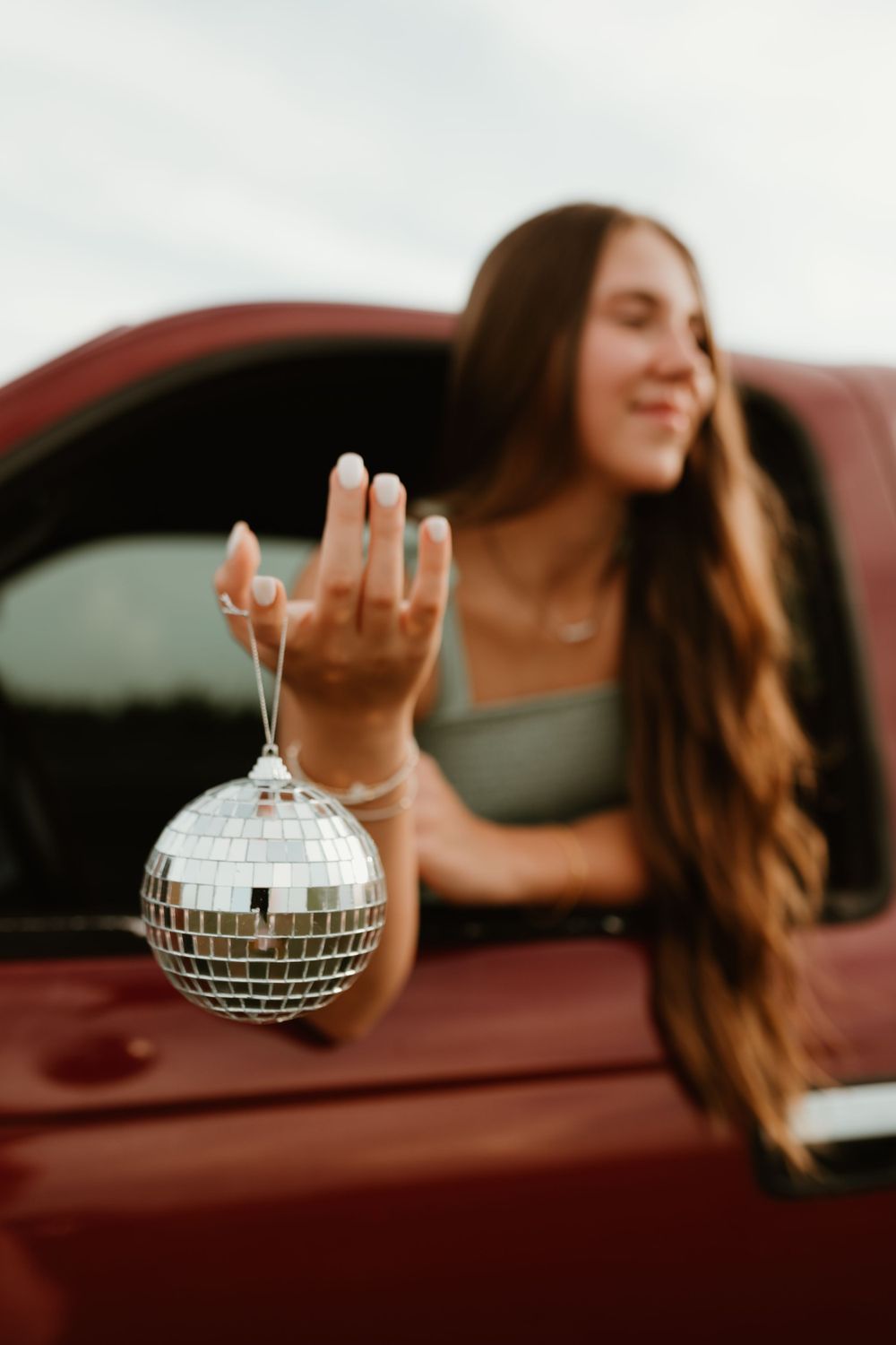 Hand holds small disco ball against red truck and sky backdrop.