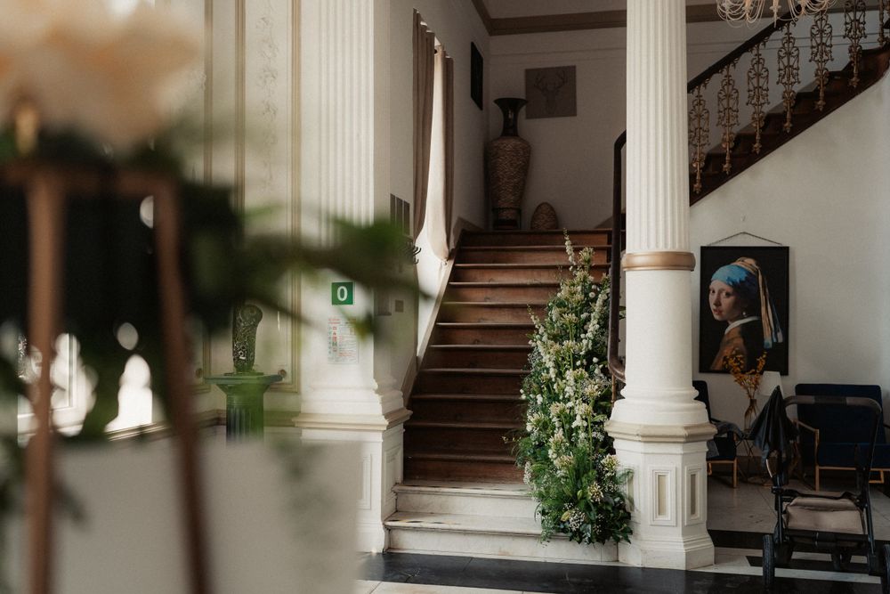 Elegant white foyer with climbing greenery adorning the wooden staircase and classic white columns.