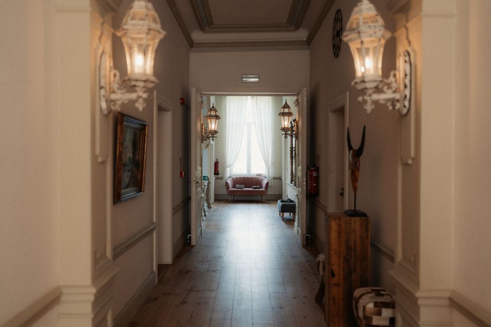 Elegant hallway with marble floors and vintage wall sconces features ornate architectural details and natural lighting.