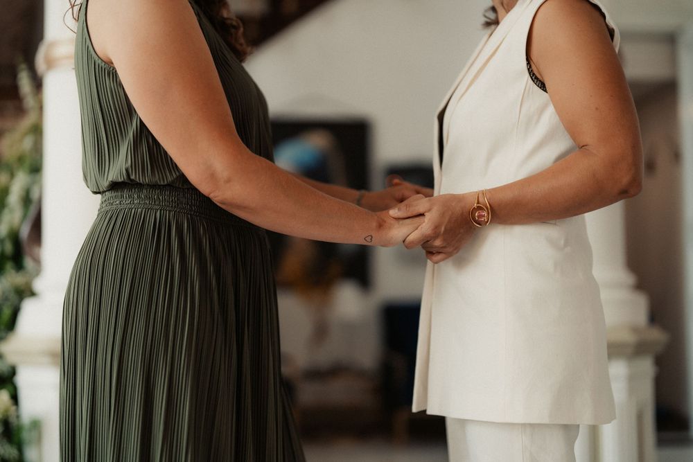 Two people holding hands while wearing contrasting dresses in olive green and white.