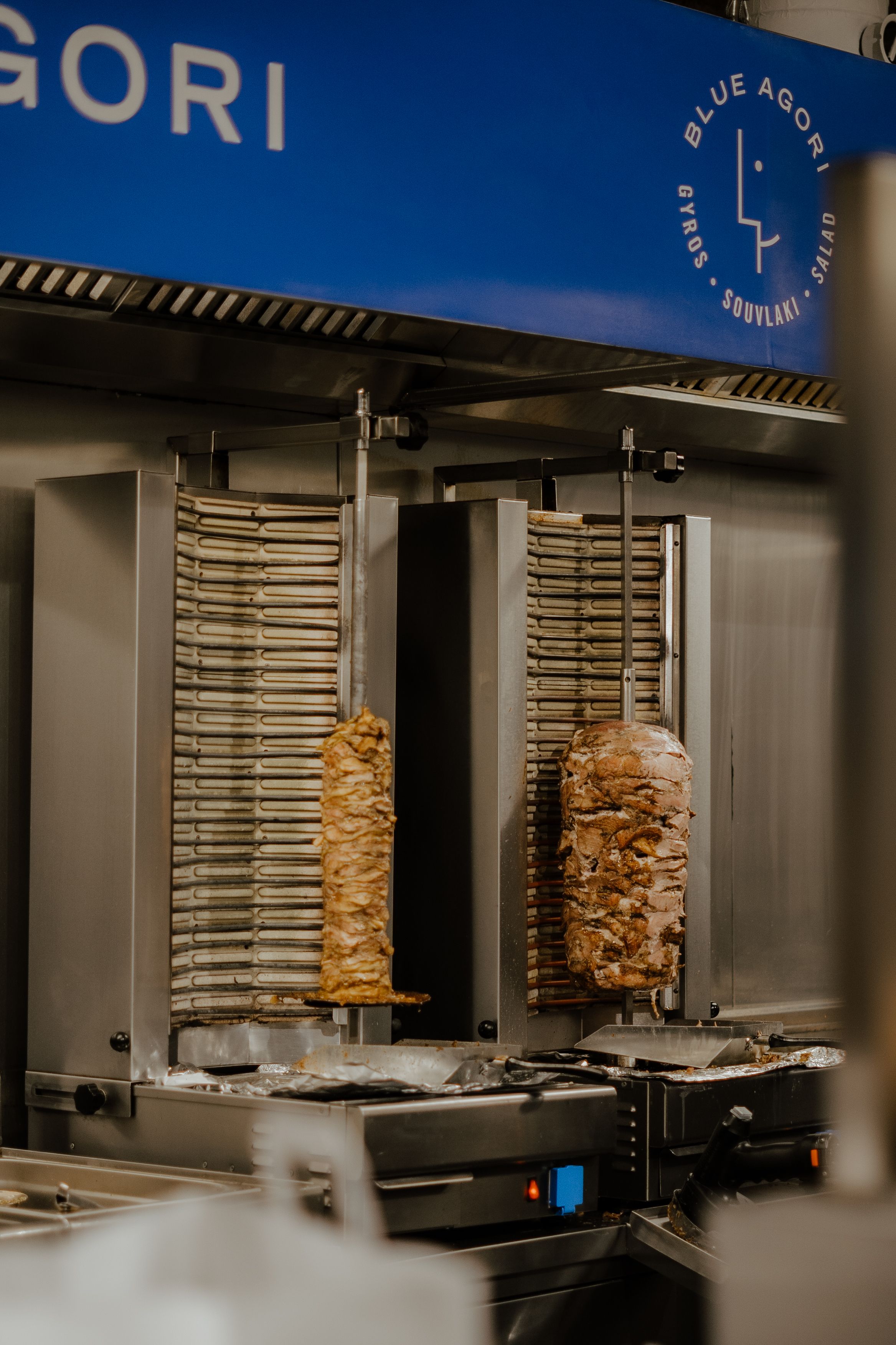 Vertical rotisserie spits with stacks of marinated meat rotating in a commercial kitchen setting.