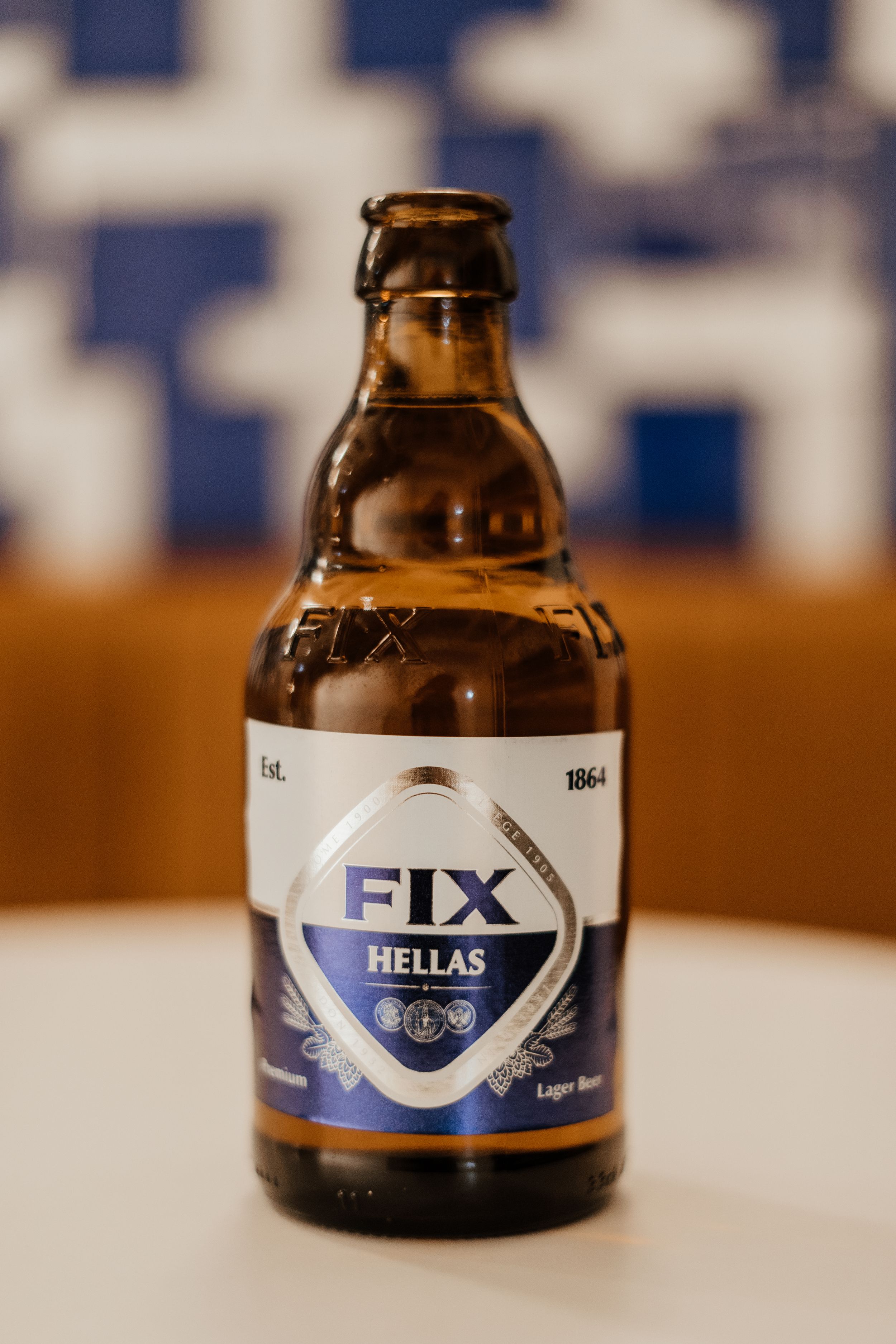 A bottle of Fix Hellas Greek beer sits on a white surface with a blue and white background.