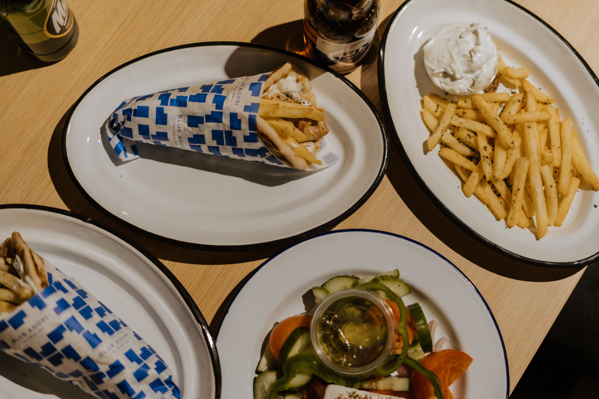 An overhead view of plates with french fries, sandwiches wrapped in blue patterned paper, and a fresh garden salad.