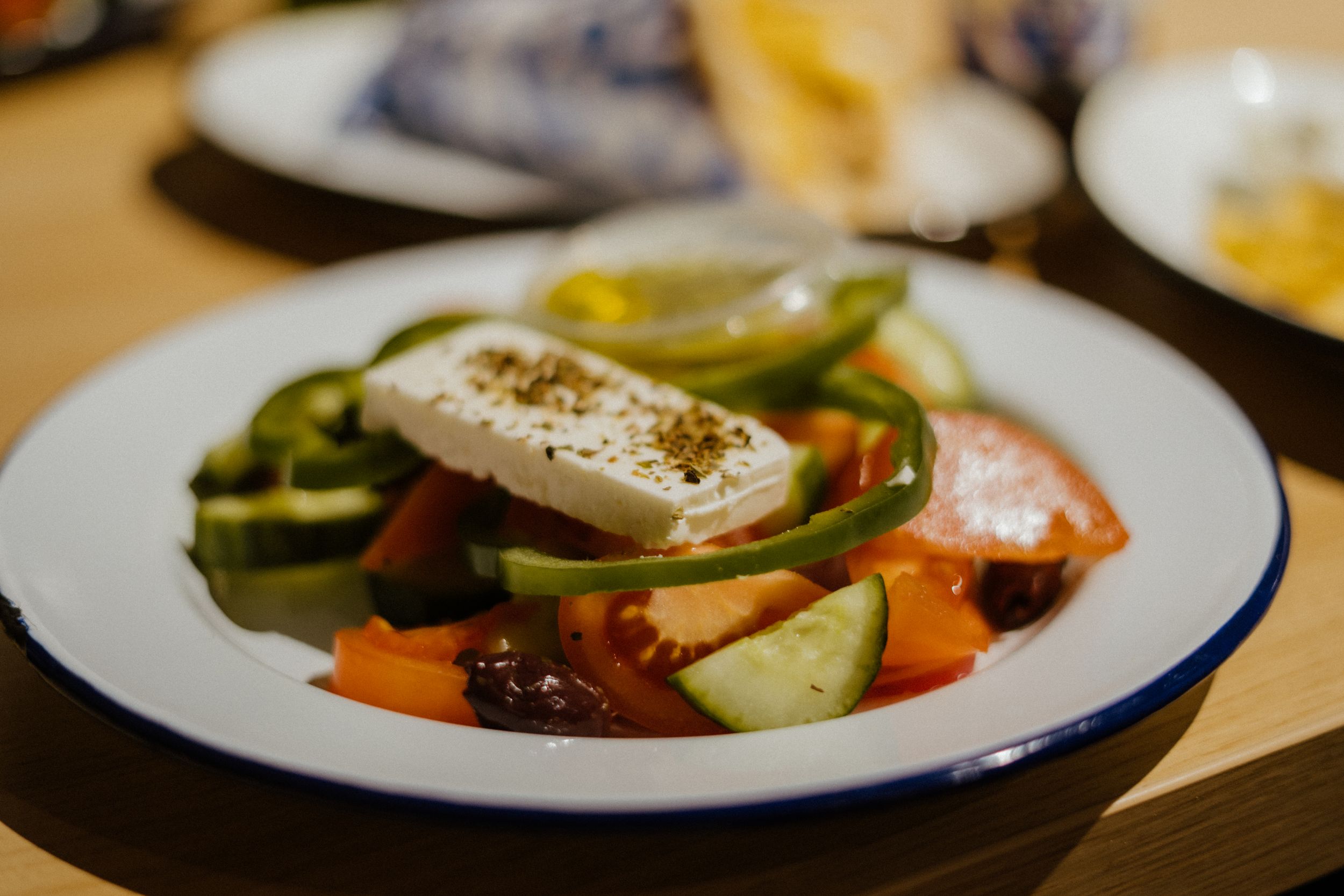 A fresh Mediterranean salad on a white plate with colorful vegetables and feta cheese drizzled with olive oil.