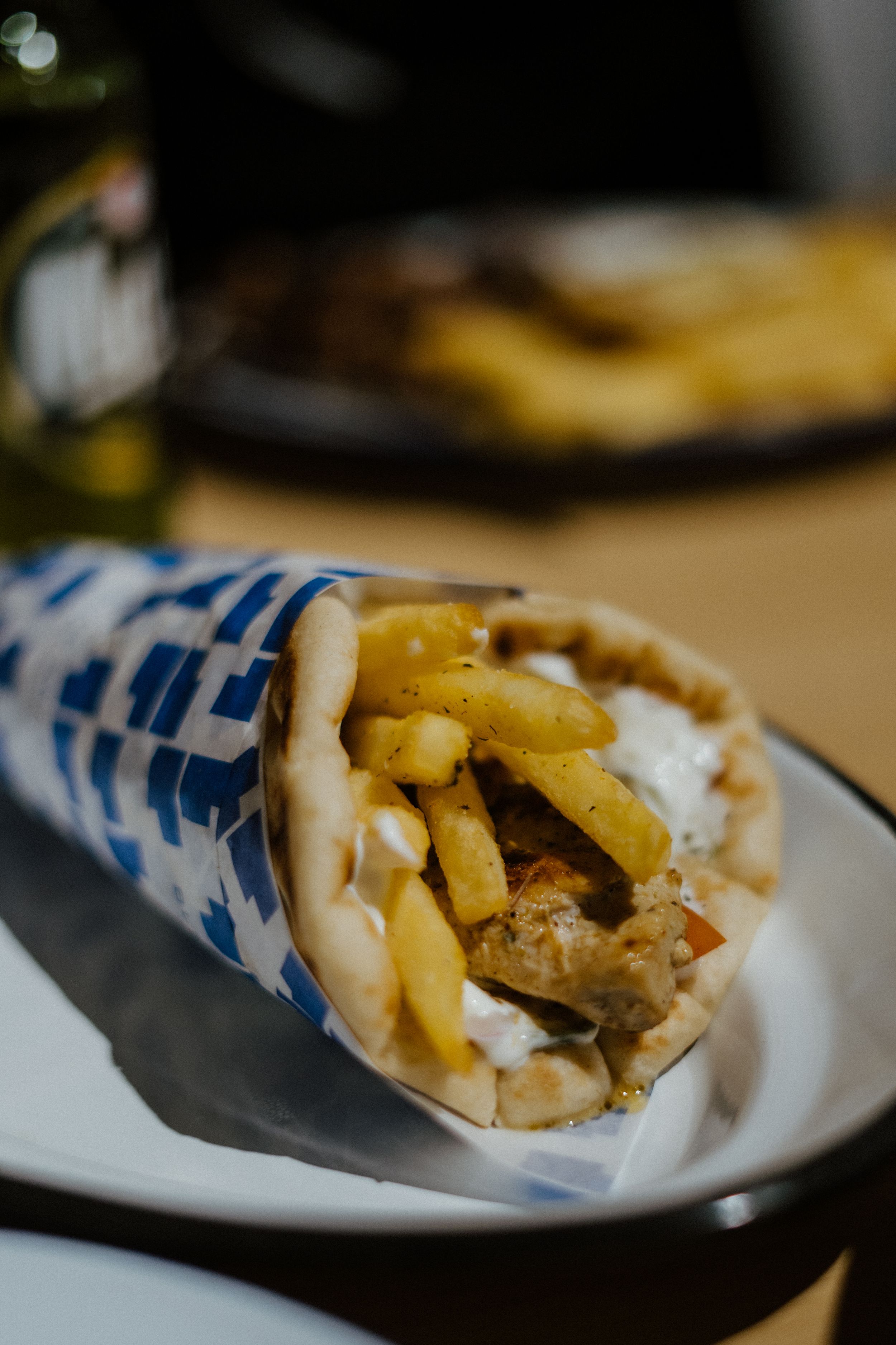 A gyro wrap filled with french fries, meat, and sauce served in blue and white checkered paper on a white plate.