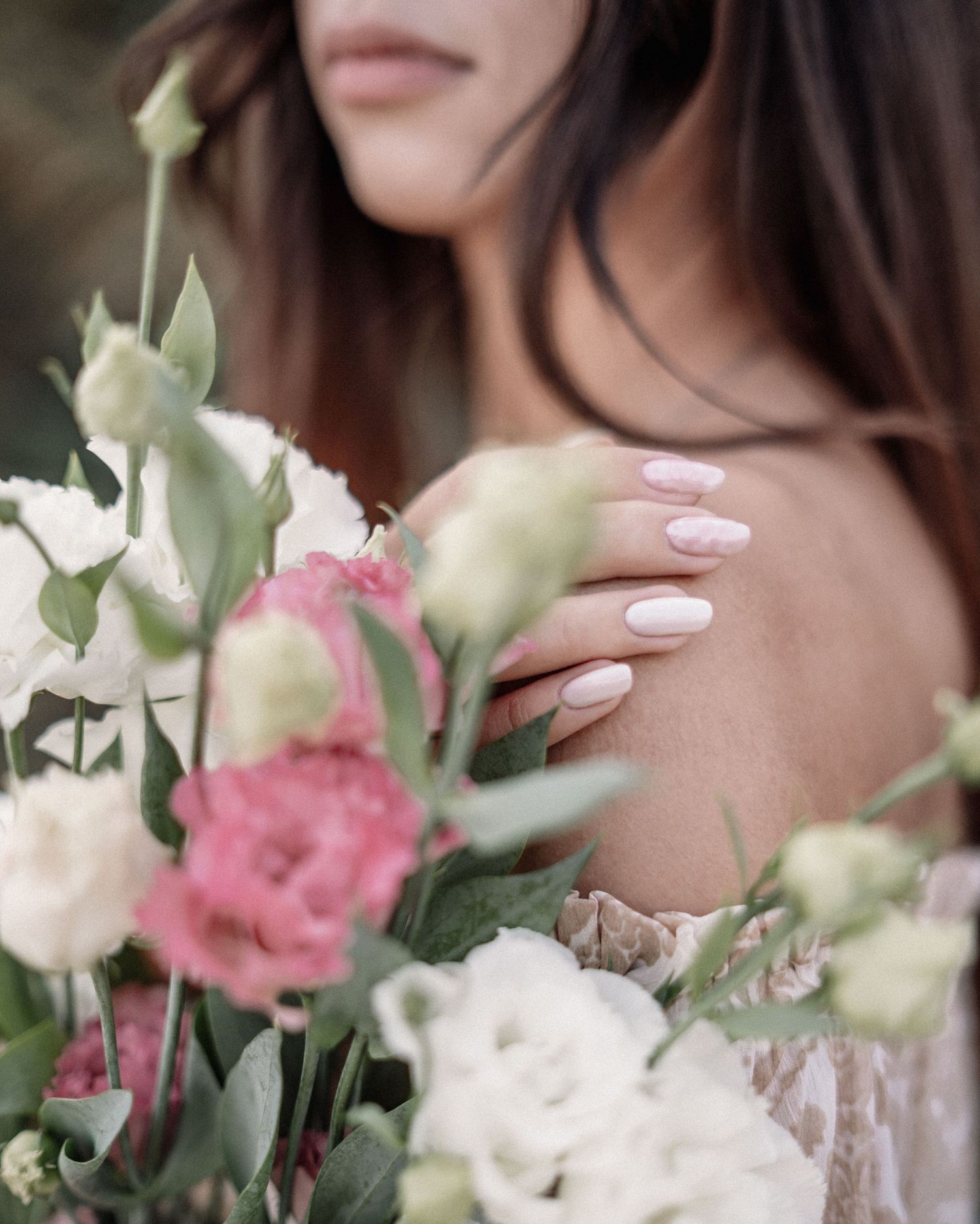 Delicate close-up of hands holding pink and white roses with manicured nails.