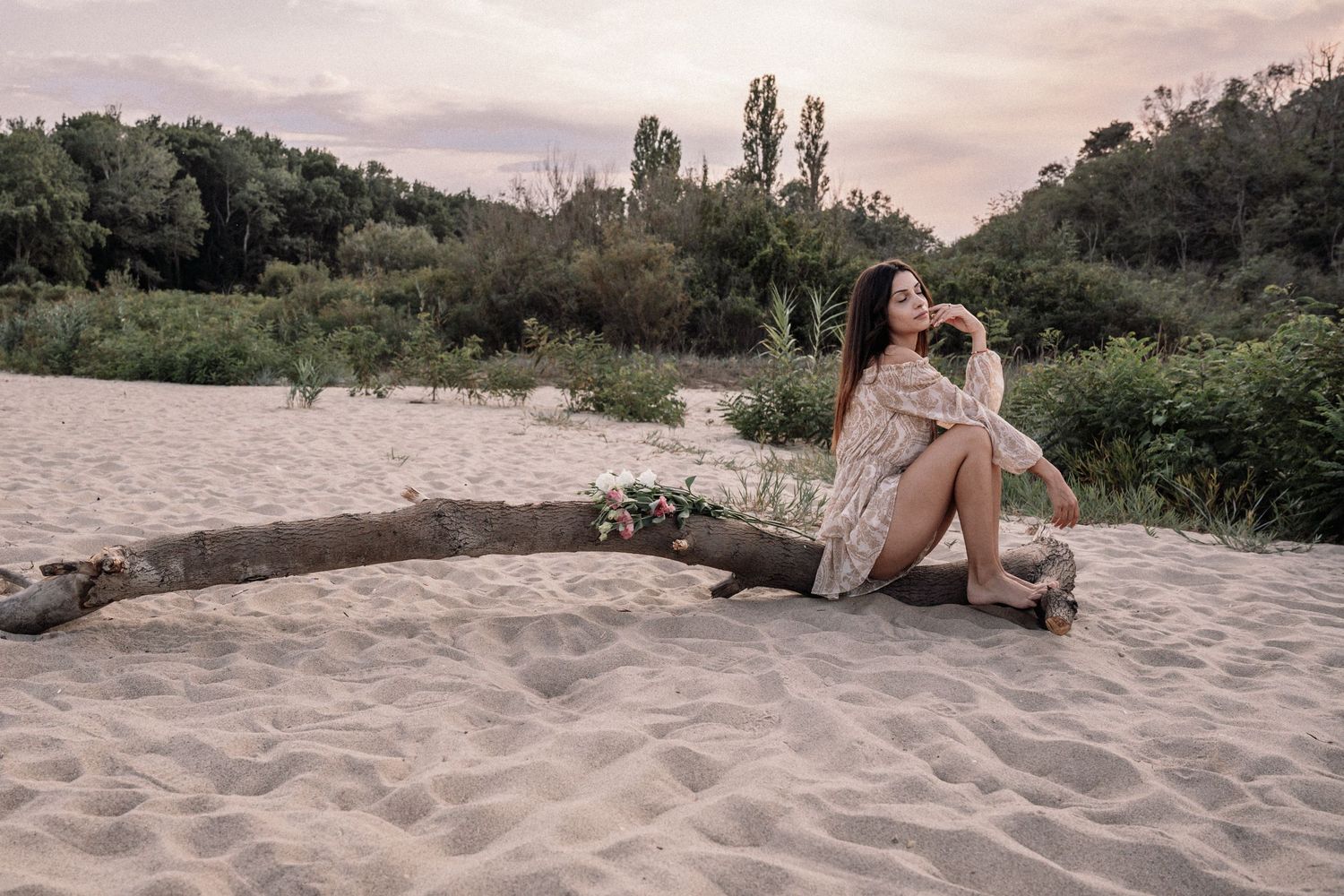 Dreamy beach photoshoot with driftwood and natural lighting at dusk.