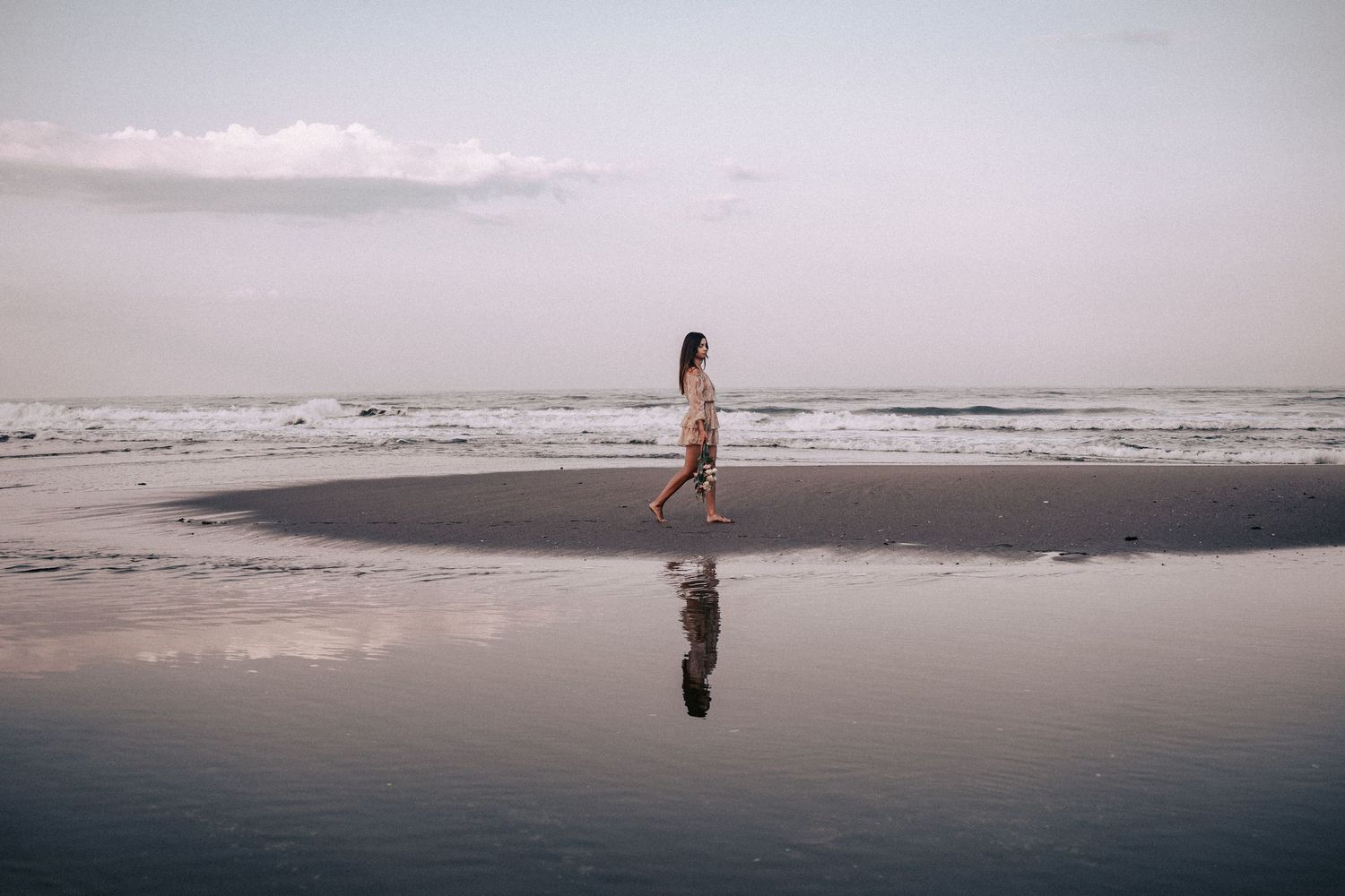 Silhouetted figure walking on reflective wet beach at sunset.