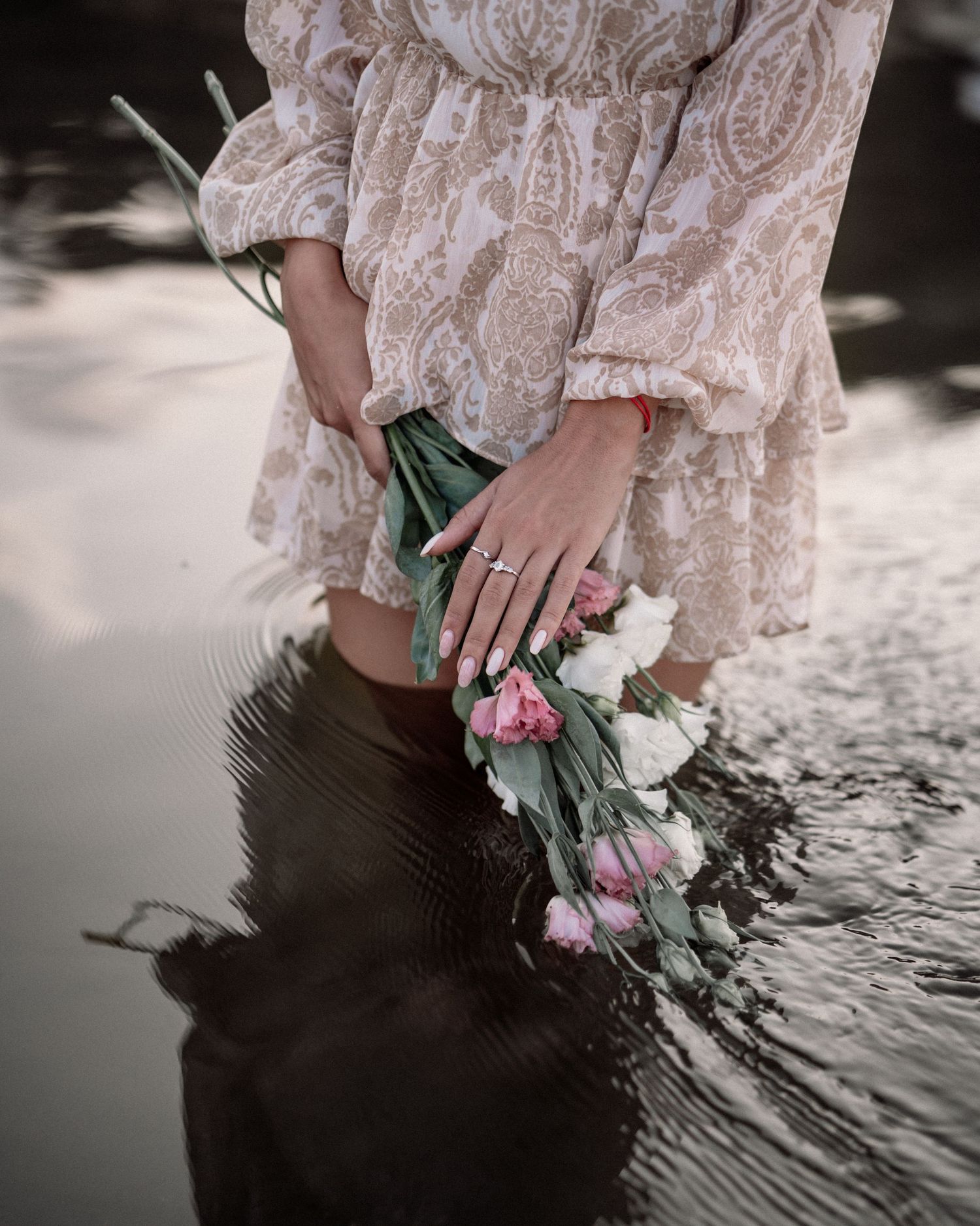 Detail shot of lace dress and floral bouquet reflected in shallow water.