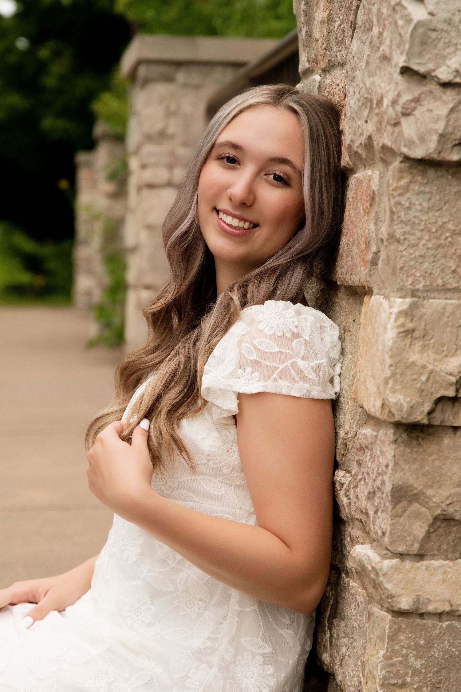 senior girl posing against a brick wall outdoors, wearing a white dress.