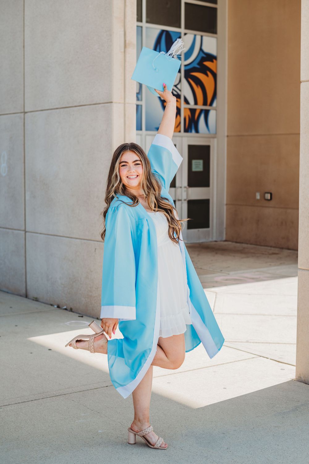 A series of graduation photos in a light blue cap and gown showing different poses against a concrete building.