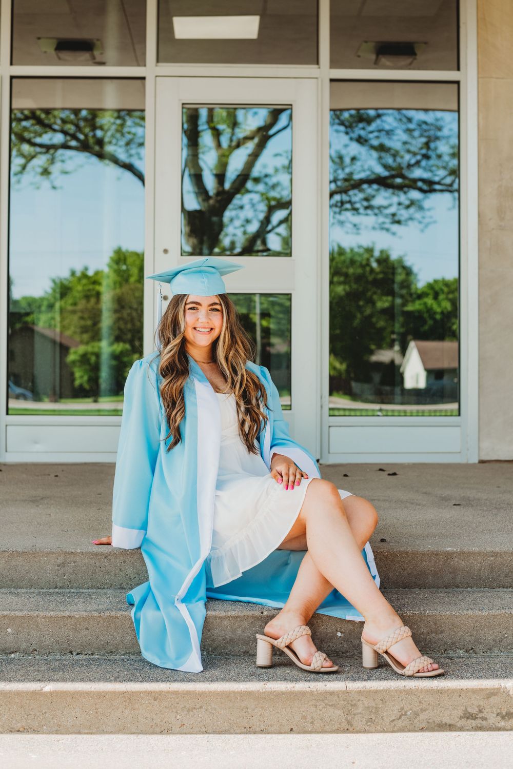 Outdoor graduation portraits featuring light blue regalia and beige heels against a building exterior.