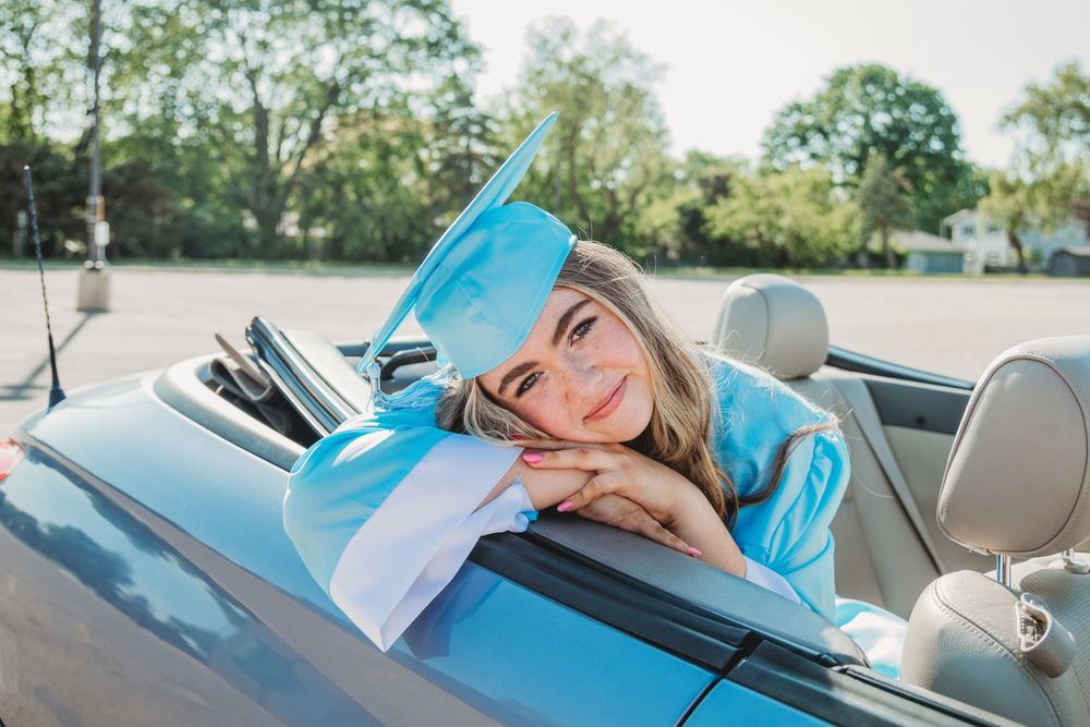 Casual graduation photo series taken in and around a car with light blue academic regalia.
