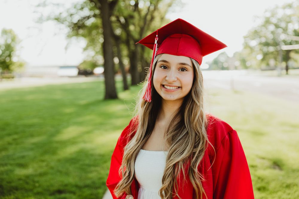 Outdoor graduation portraits in traditional red cap and gown against a green landscape.