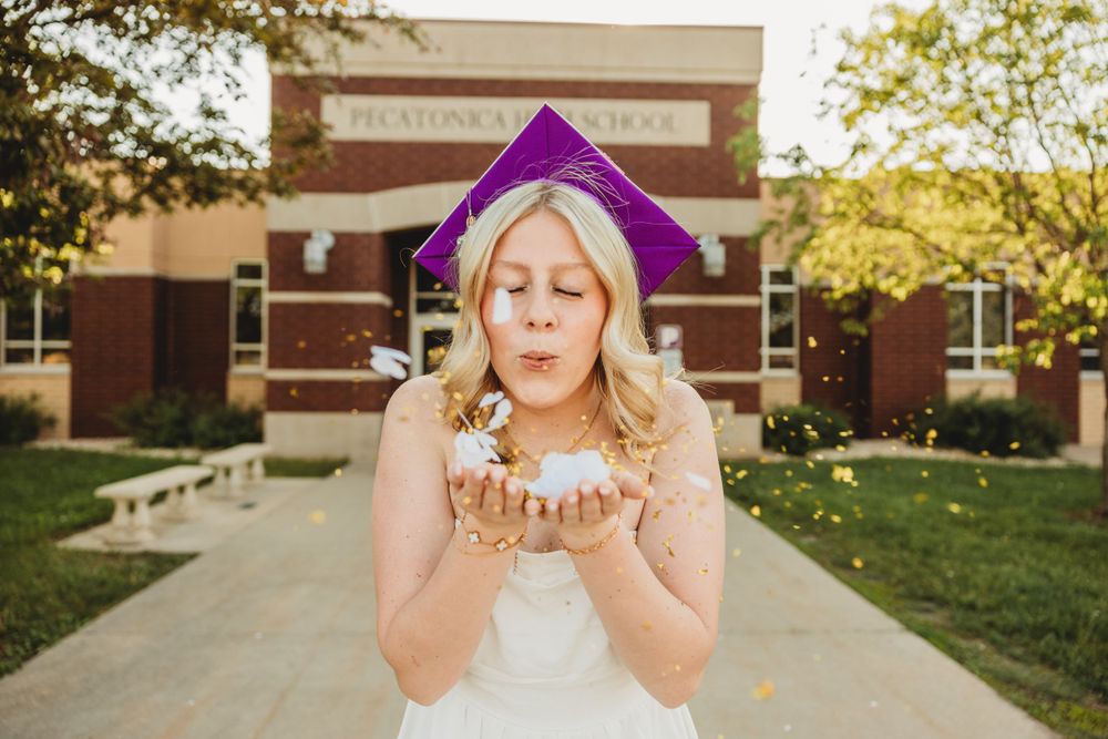 Celebratory graduation photos with glitter toss in front of brick school building.