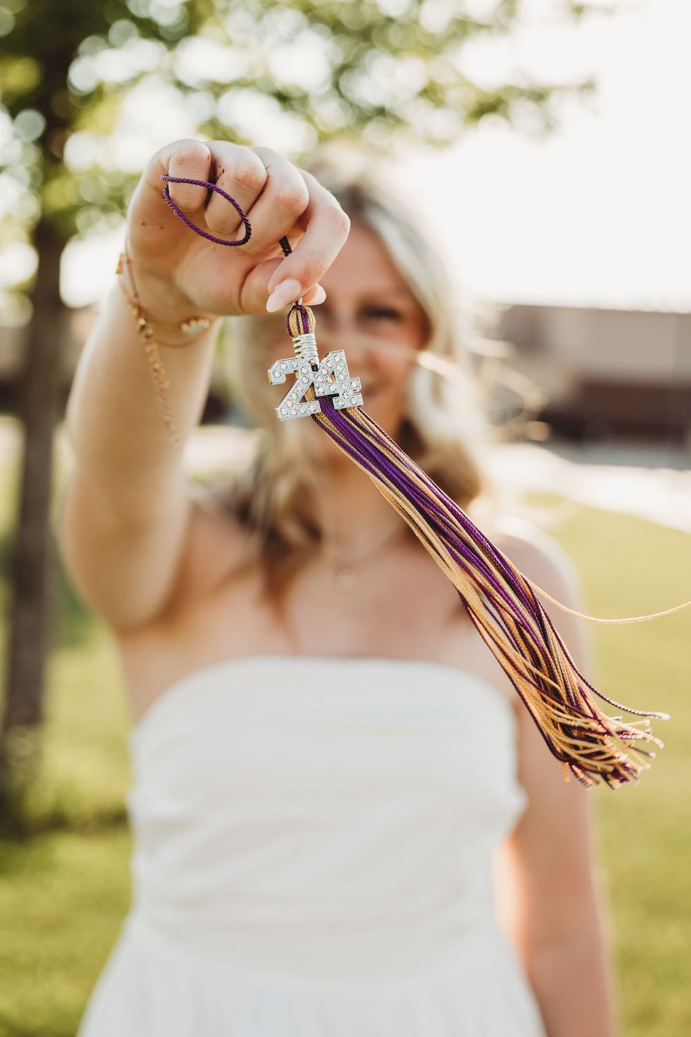 Detail shot of graduation tassel with purple and gold colors being held up in sunlight.