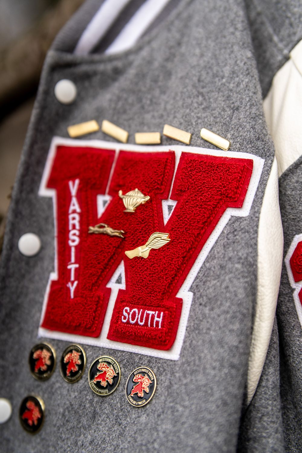 Gray varsity letterman jacket with red W patch, gold pins, and South embroidery detail.