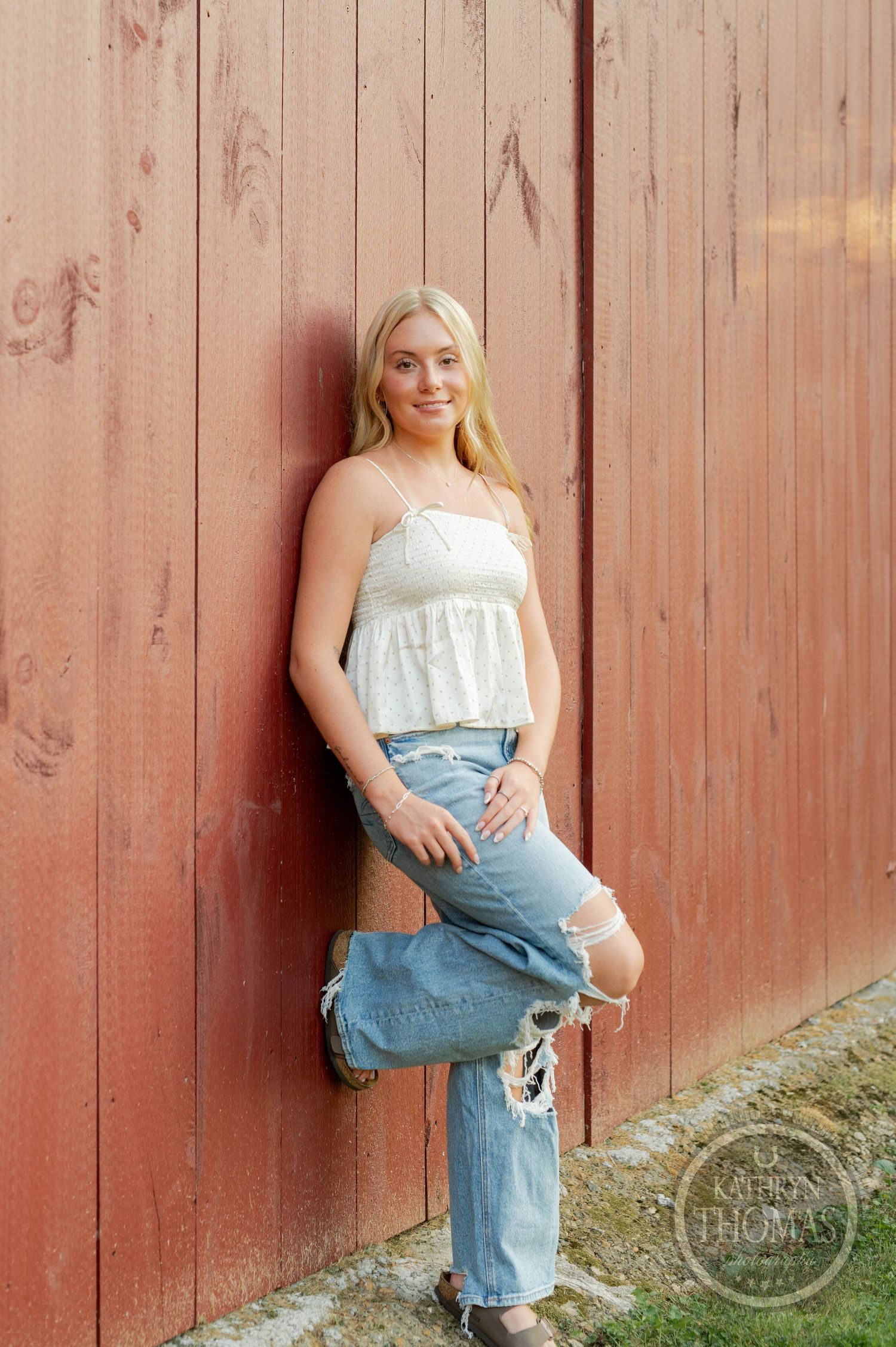 Casual summer portrait against a red barn wall wearing distressed jeans and a white top.