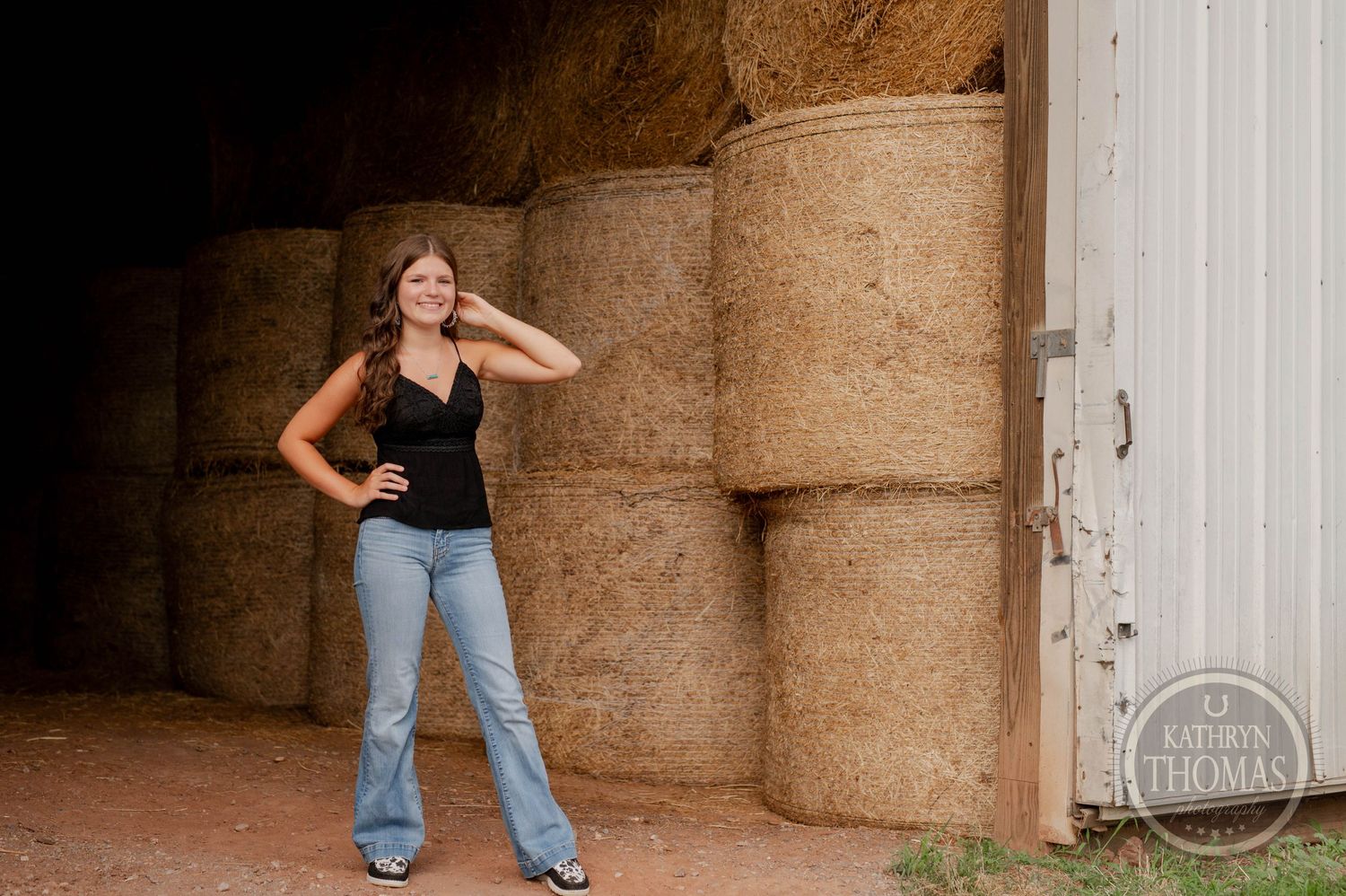 Casual pose by hay bales and white door in rustic barn setting.